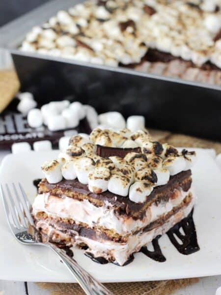 Close up of a slice of smores icebox cake with the rest of the cake in the background.