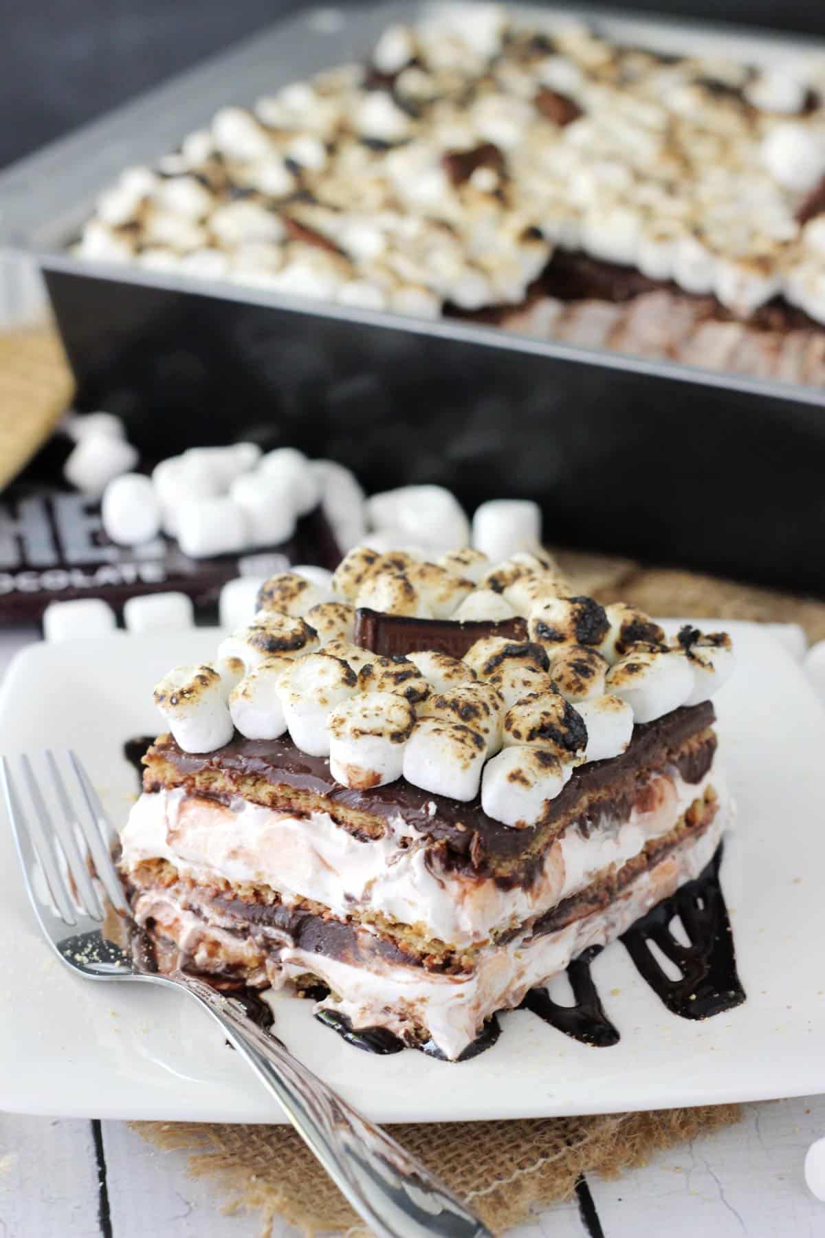 Close up of a slice of smores icebox cake with the rest of the cake in the background.