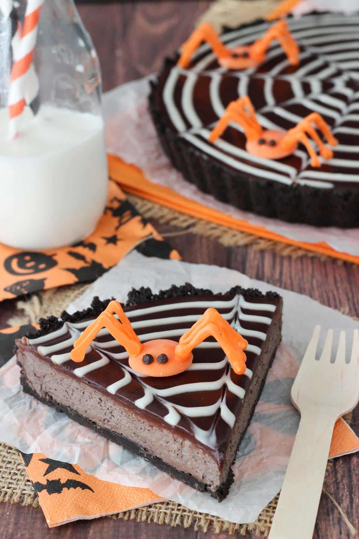 A slice of spiderweb chocolate tart with a candy spider on top and the rest of the tart in the background.