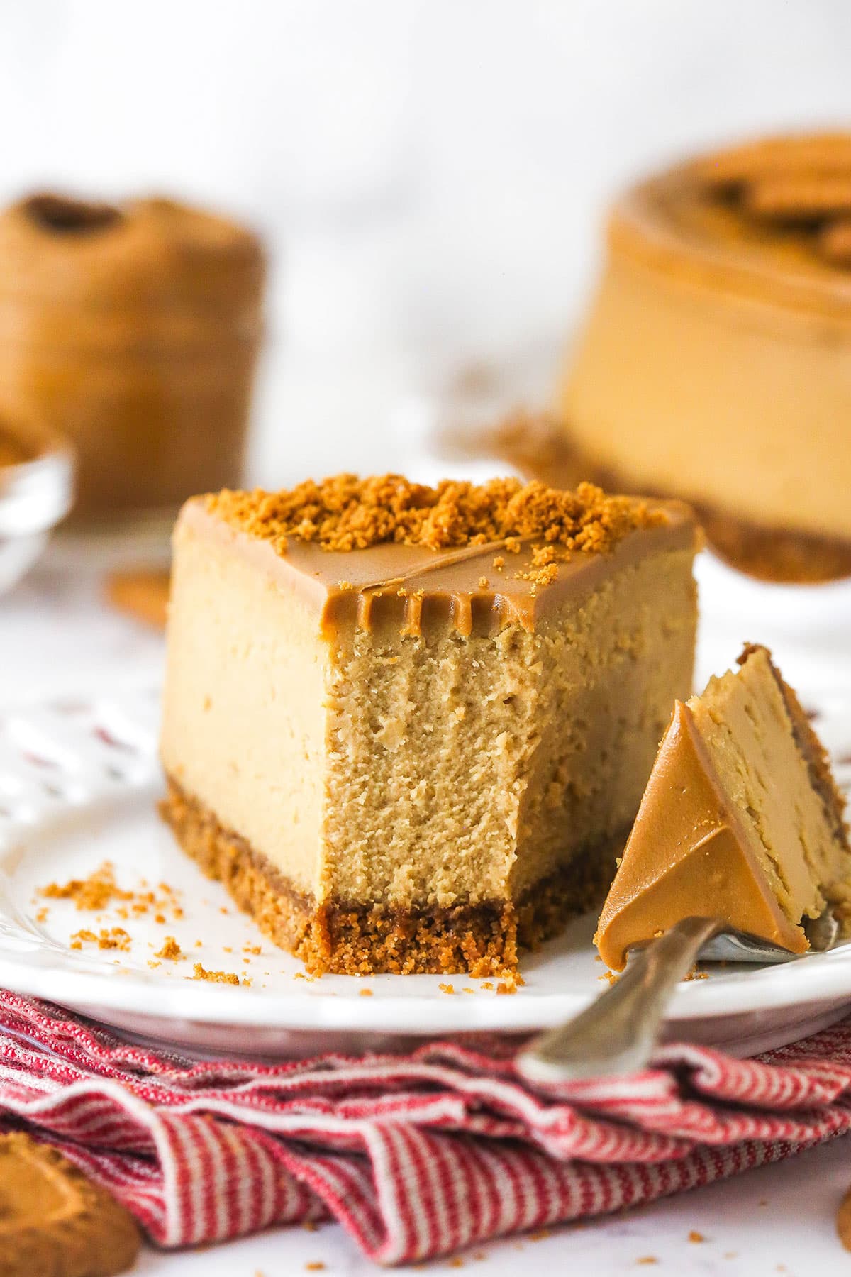 With a Biscoff cookie crust and cookie spread in the filling, this Biscoff Cheesecake tastes just like the cookies. Front view of a slice of Biscoff cheesecake on a plate with a bite on the fork next to it
