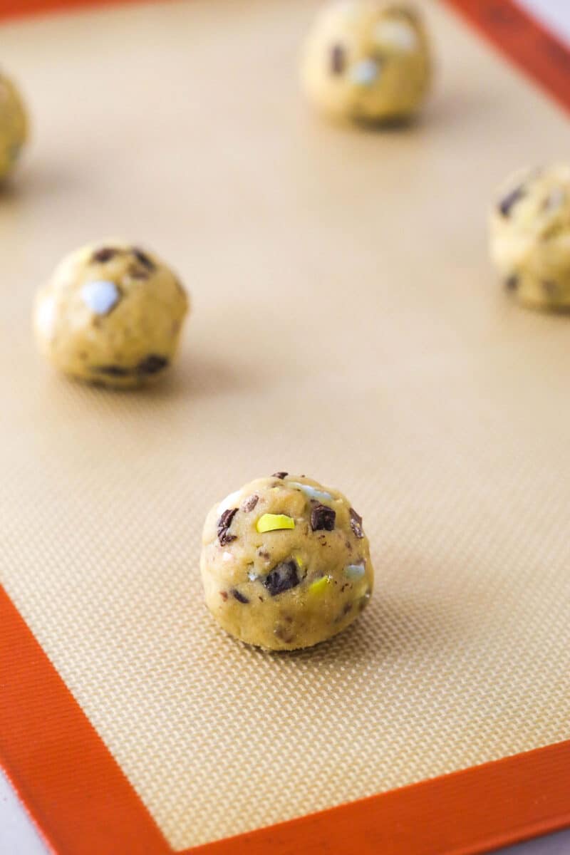 Every bite of these soft and chewy Cadbury egg cookies is dotted with crushed Cadbury eggs and chocolate. Perfect for spring & Easter! Cadbury egg cookie dough balls on a baking sheet