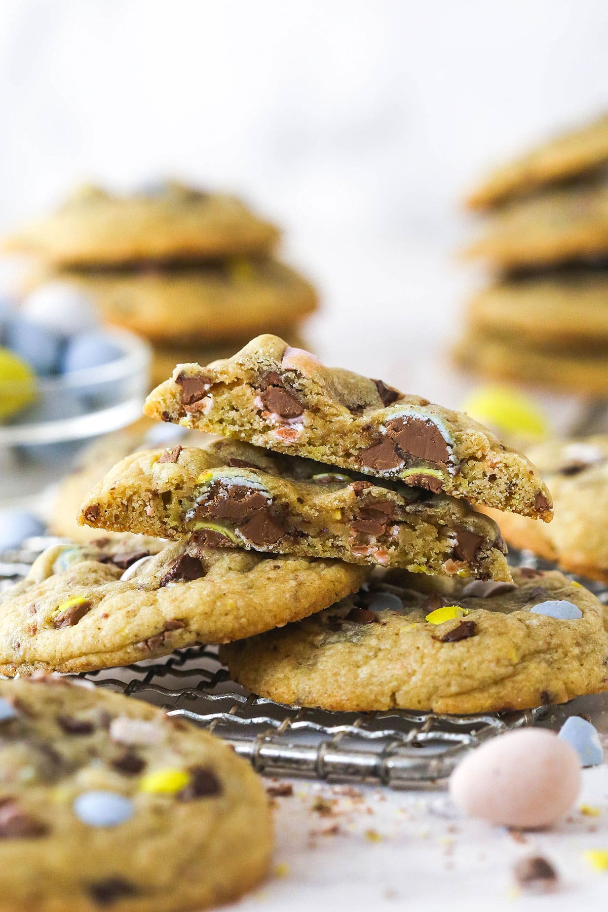 Every bite of these soft and chewy Cadbury egg cookies is dotted with crushed Cadbury eggs and chocolate. Perfect for spring & Easter! Cadbury egg cookies on a cooling rack, one cut in half to show the inside