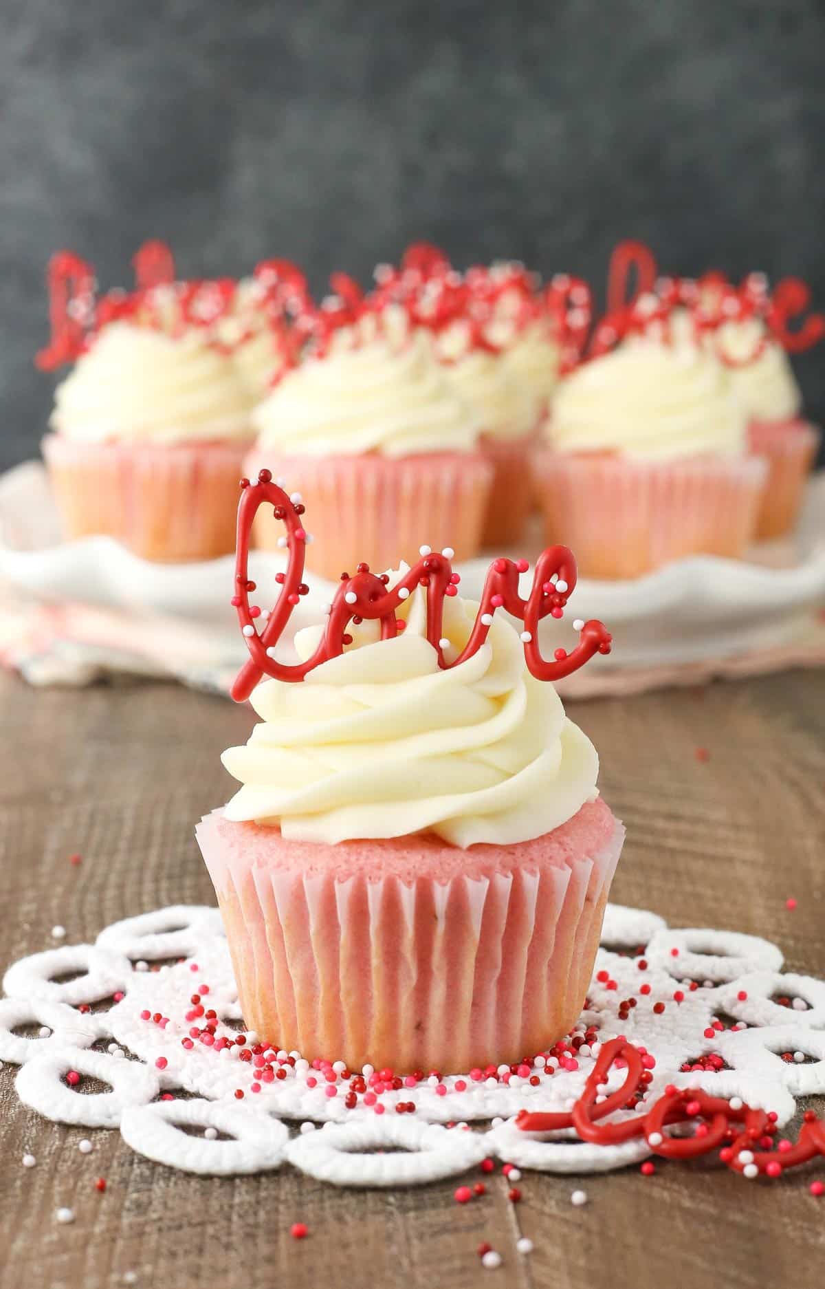 Close up of a strawberry cupcake with cream cheese frosting with more cupcakes in the background.