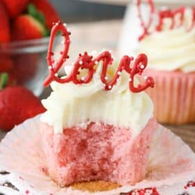 Close up of a strawberry cupcake with cream cheese frosting with a bite removed.