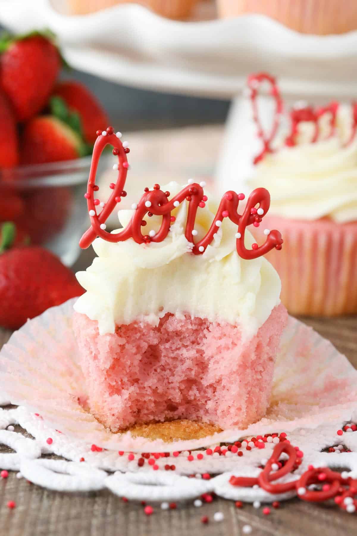 Close up of a strawberry cupcake with cream cheese frosting with a bite removed.