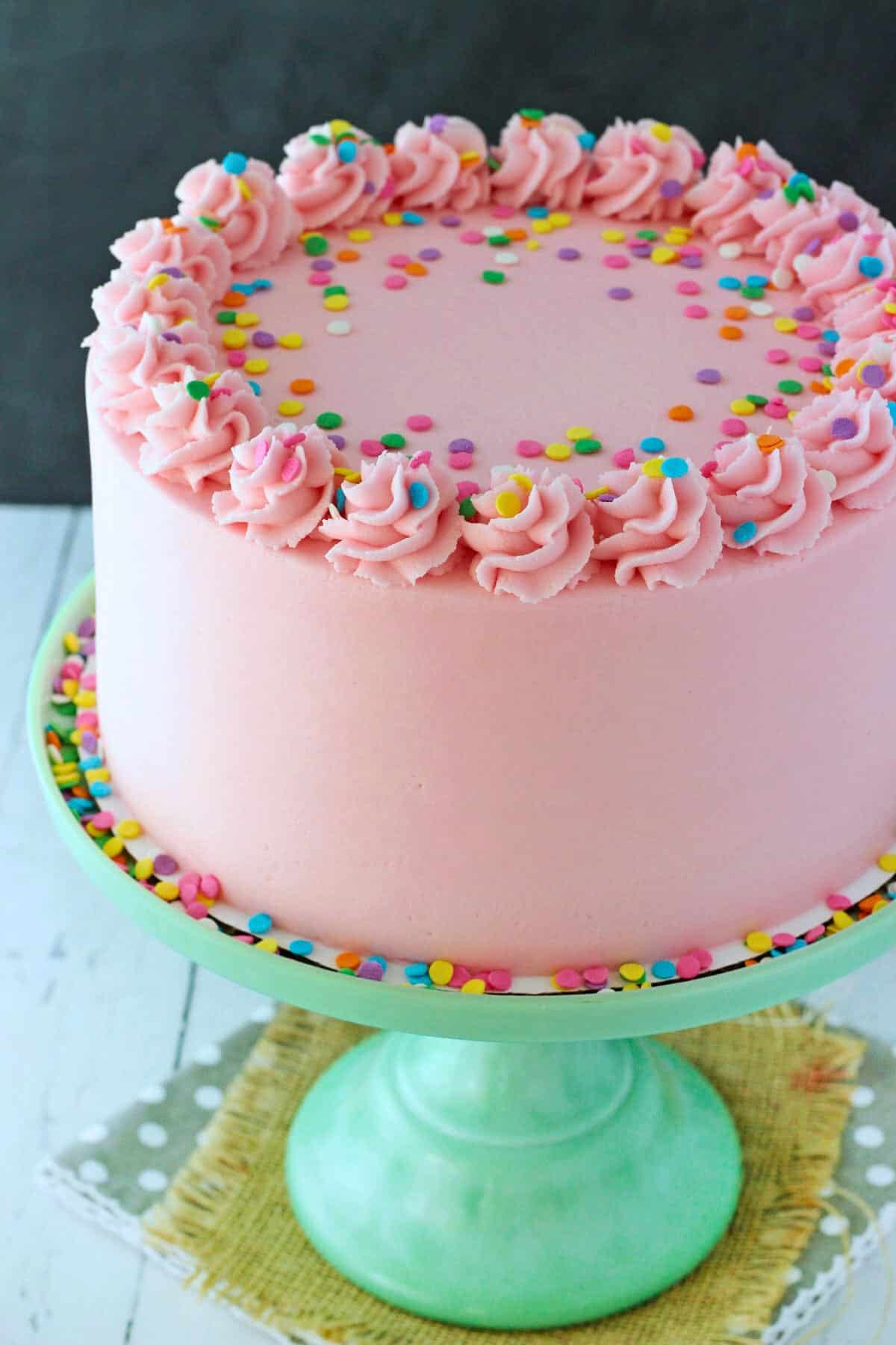 Close up of a vanilla cake frosted in pink on a light green cake stand.