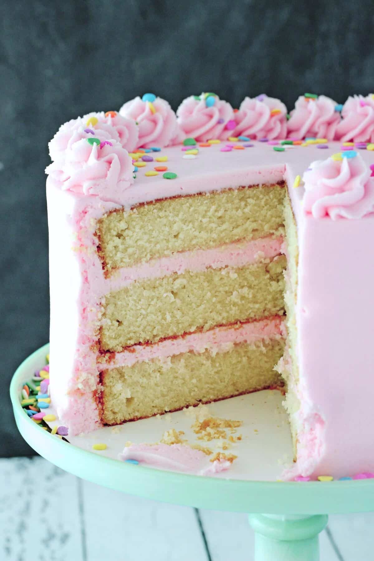 Close up of a vanilla cake frosted in pink with a few slices removed to show center.