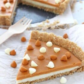Close up of a slice of white chocolate butterscotch tart with the rest of the tart in the background.