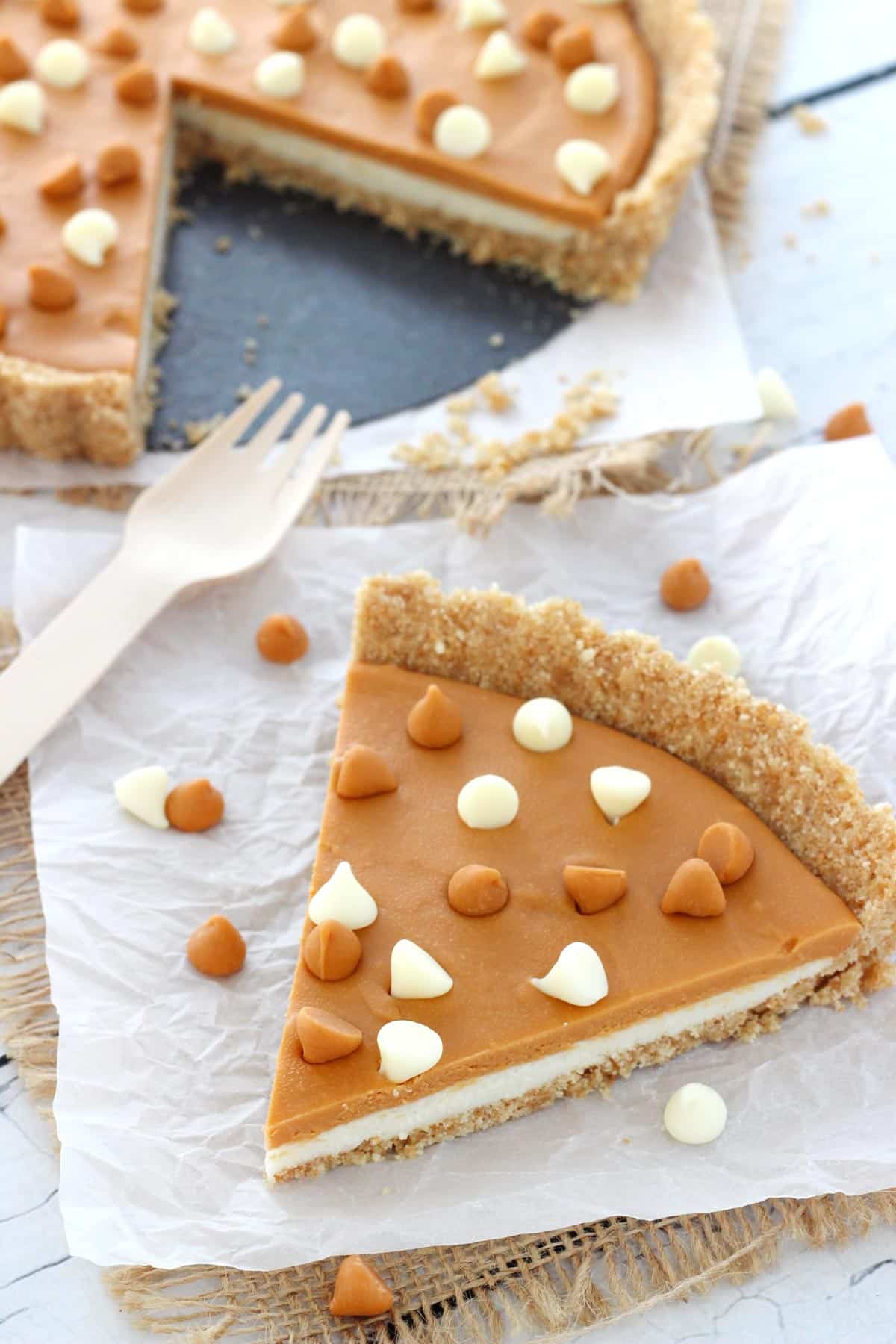 A slice of white chocolate butterscotch tart with the rest of the tart in the background.