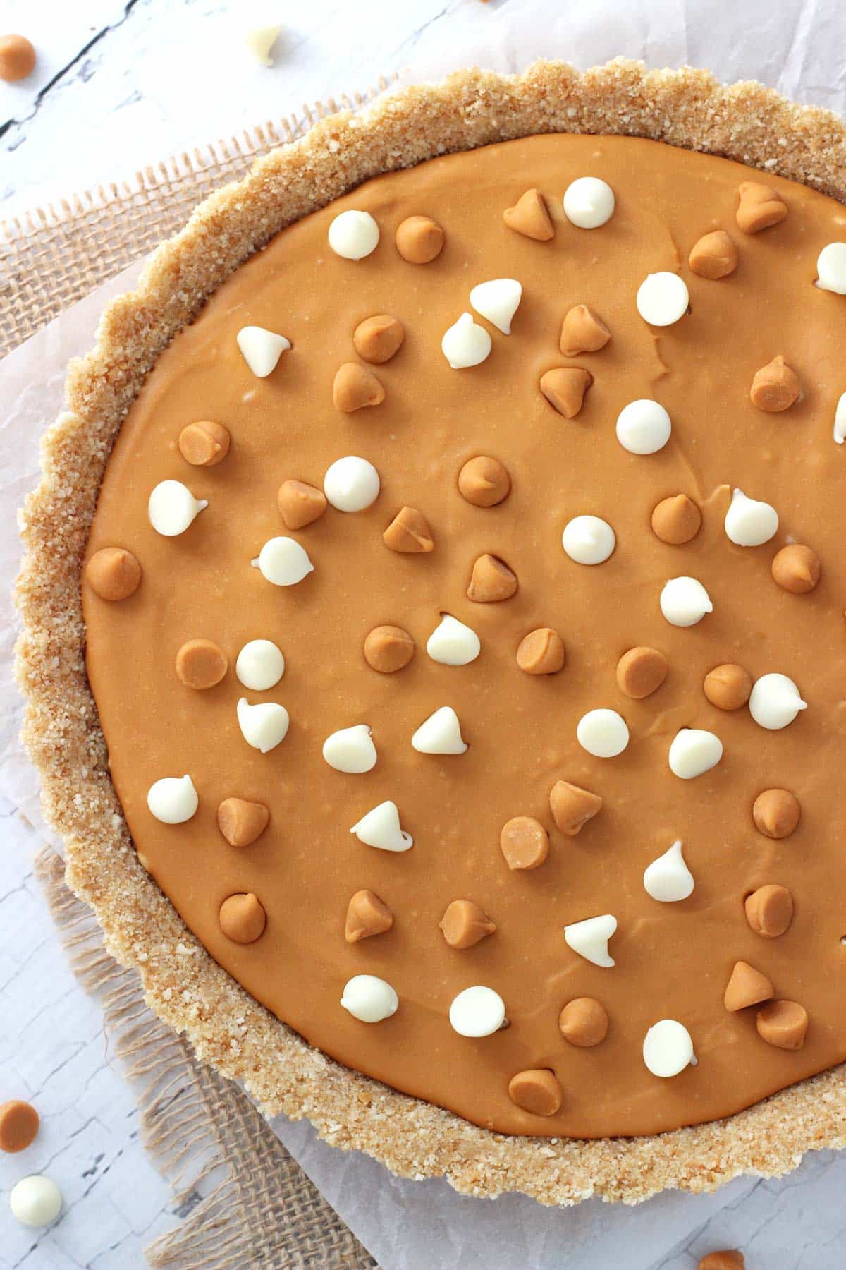 Overhead view of half of a white chocolate butterscotch tart on a piece of parchment and burlap.