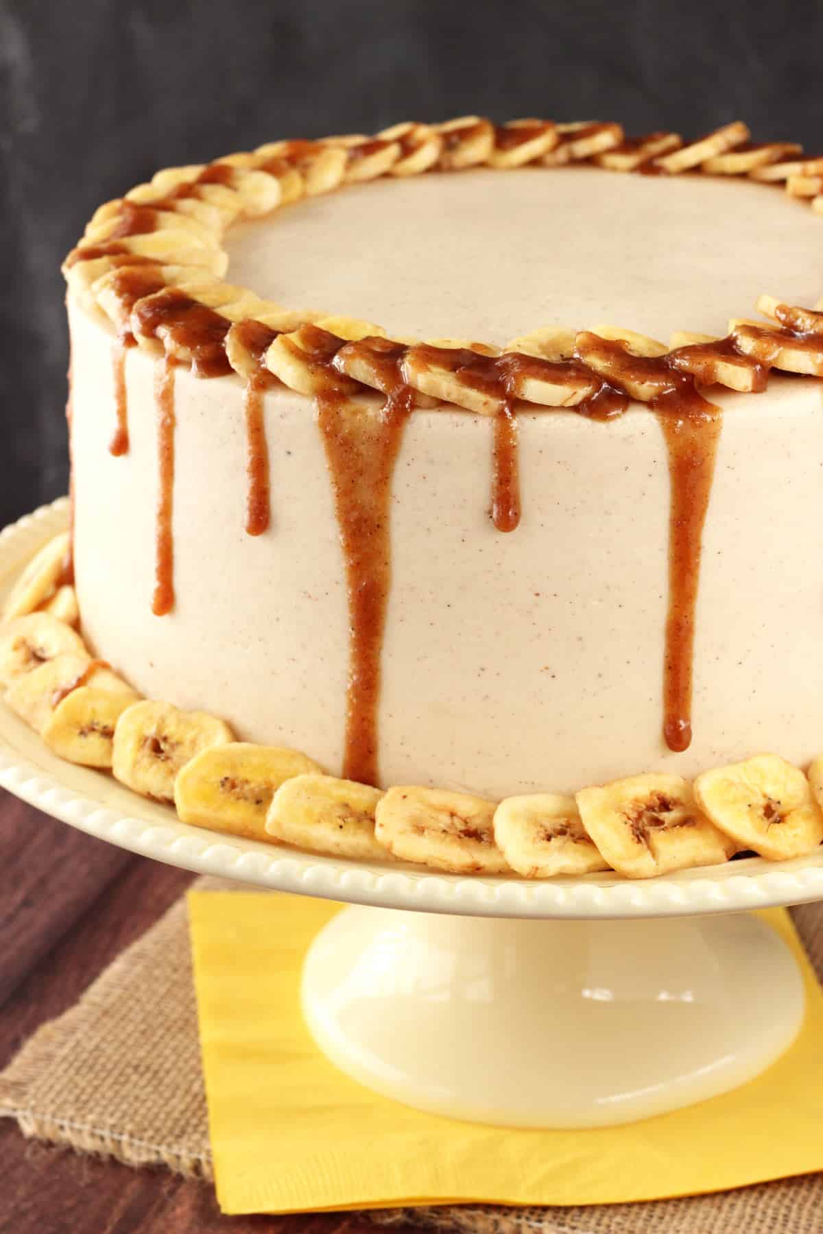 Close up of a bananas foster layer cake on a cream colored cake stand.
