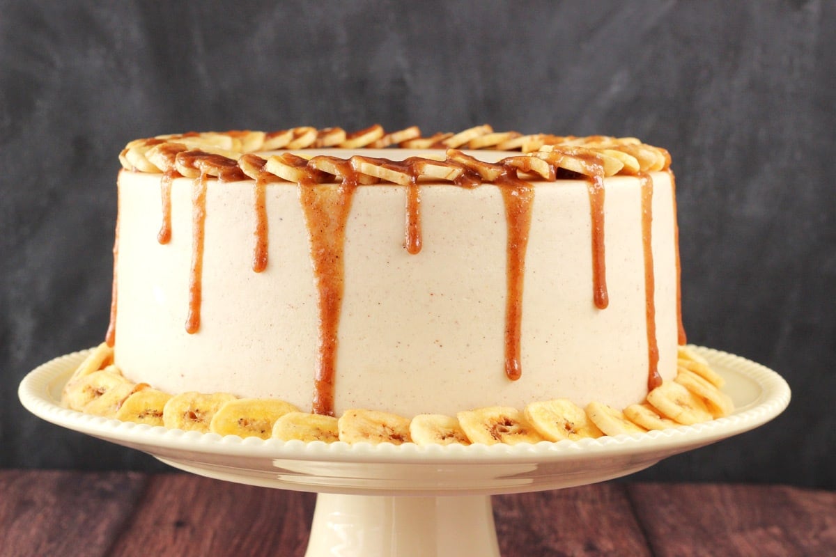 Close up of a bananas foster layer cake on a cream colored cake stand.