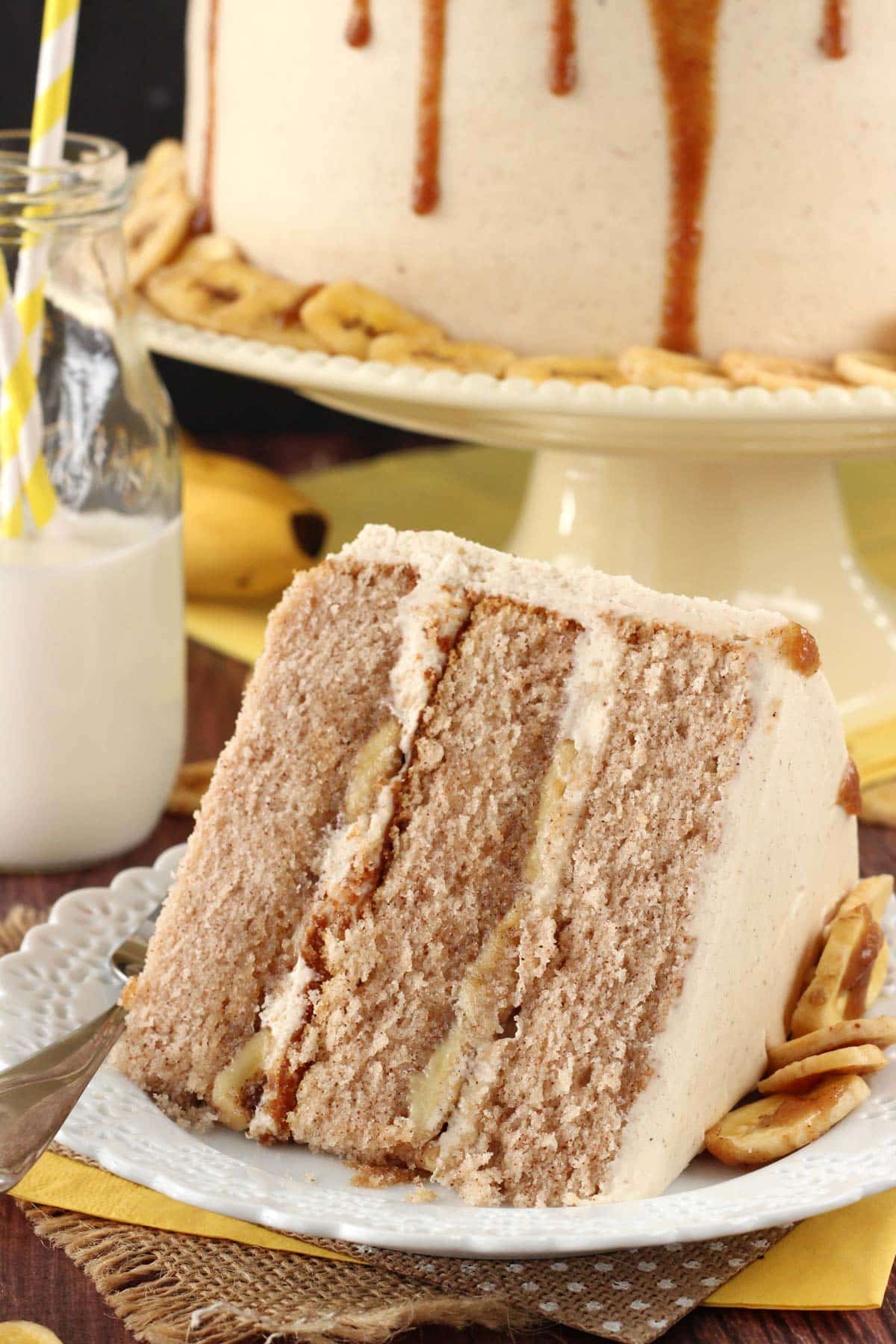 Close up of a slice of bananas foster layer cake on a small white plate with the rest of the cake in the background.