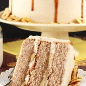 Close up of a slice of bananas foster layer cake on a small white plate with the rest of the cake in the background.