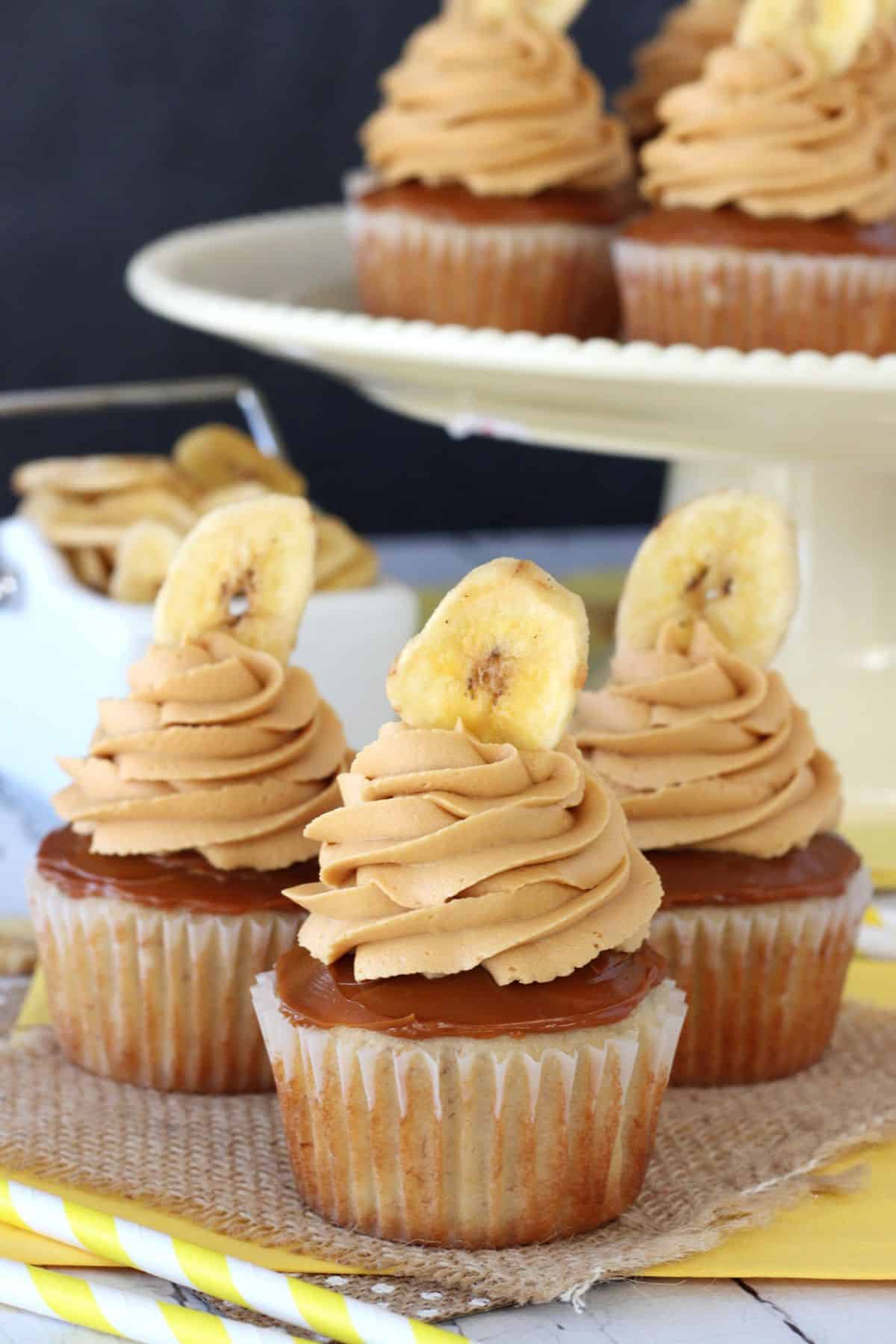 Three banoffee cupcakes on a piece of burlap with more cupcakes in the background.