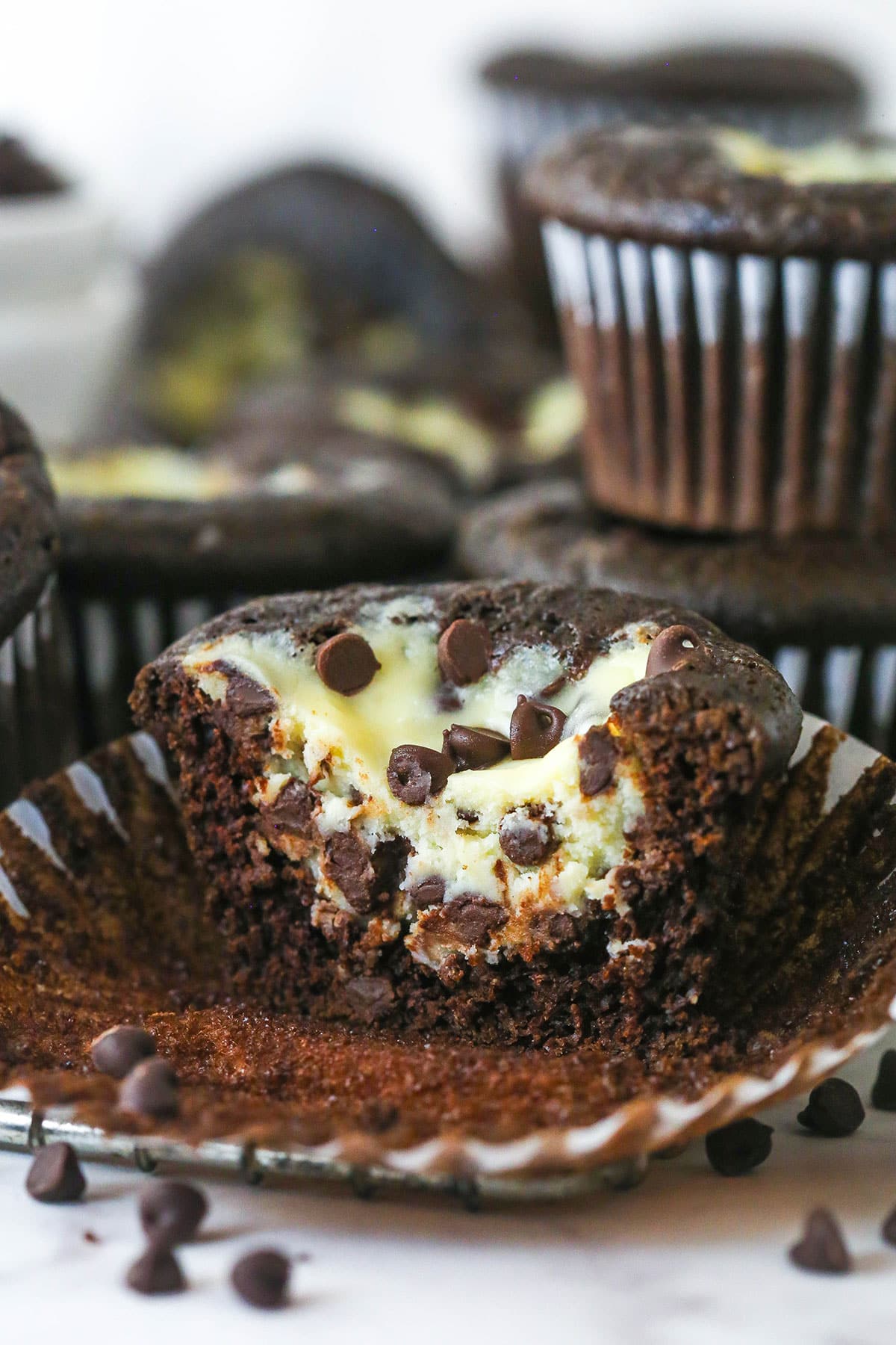These Black Bottom Cupcakes combine two desserts in one with a rich chocolate cupcake and a creamy chocolate chip cheesecake filling. A black bottom cupcake with the wrapper pulled down and a bite missing to show the inside