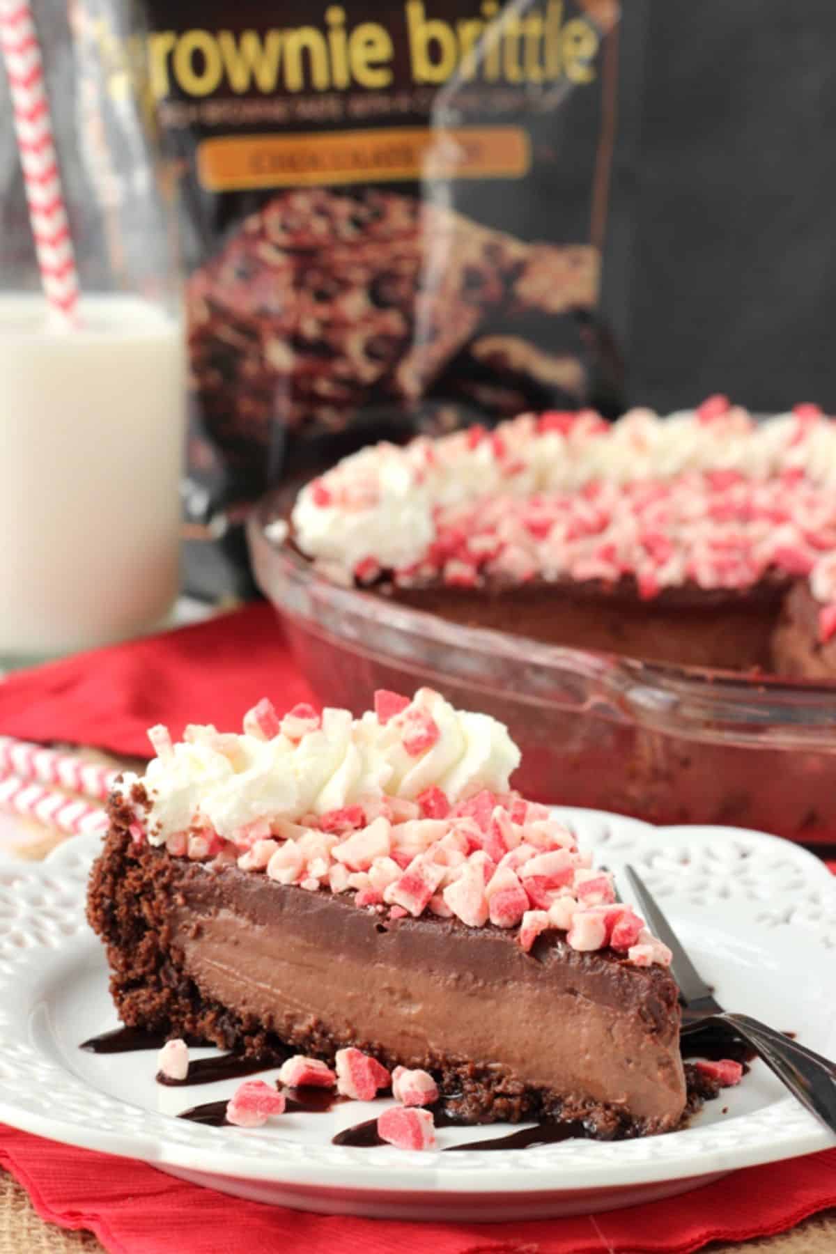 A slice of Brownie Brittle peppermint chocolate pie on a white plate with the rest of the pie in the background.