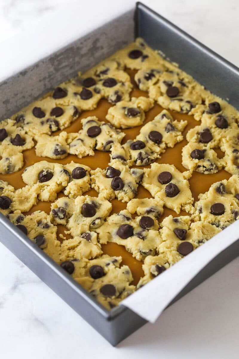 These Caramel Cookie Bars combine gooey caramel and chewy chocolate chip cookies in one perfect dessert. Easy to make! Chocolate chip cookie dough on top of melted caramel in a square pan