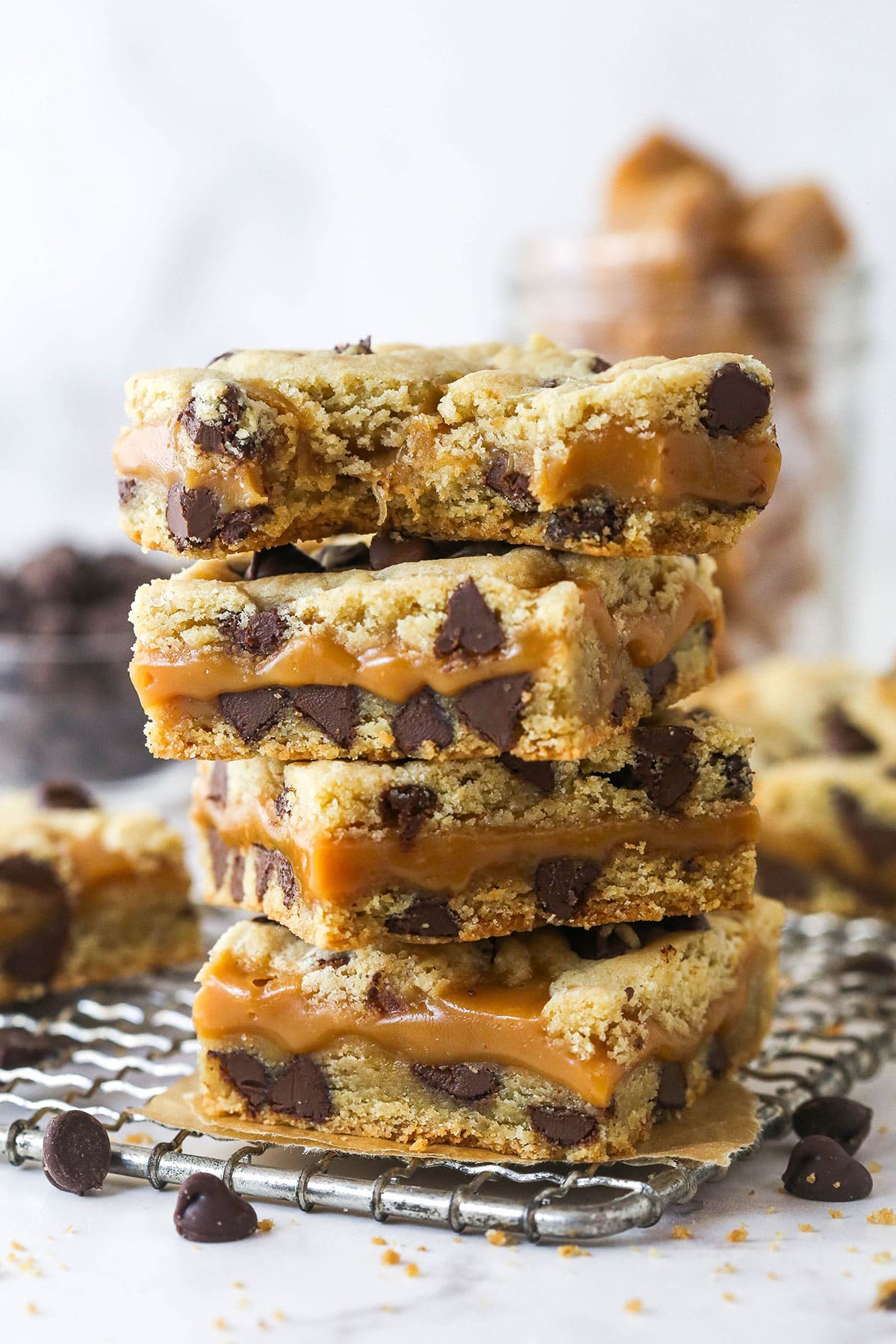 These Caramel Cookie Bars combine gooey caramel and chewy chocolate chip cookies in one perfect dessert. Easy to make! Four caramel cookie bars stacked on a towel, one with a bite missing