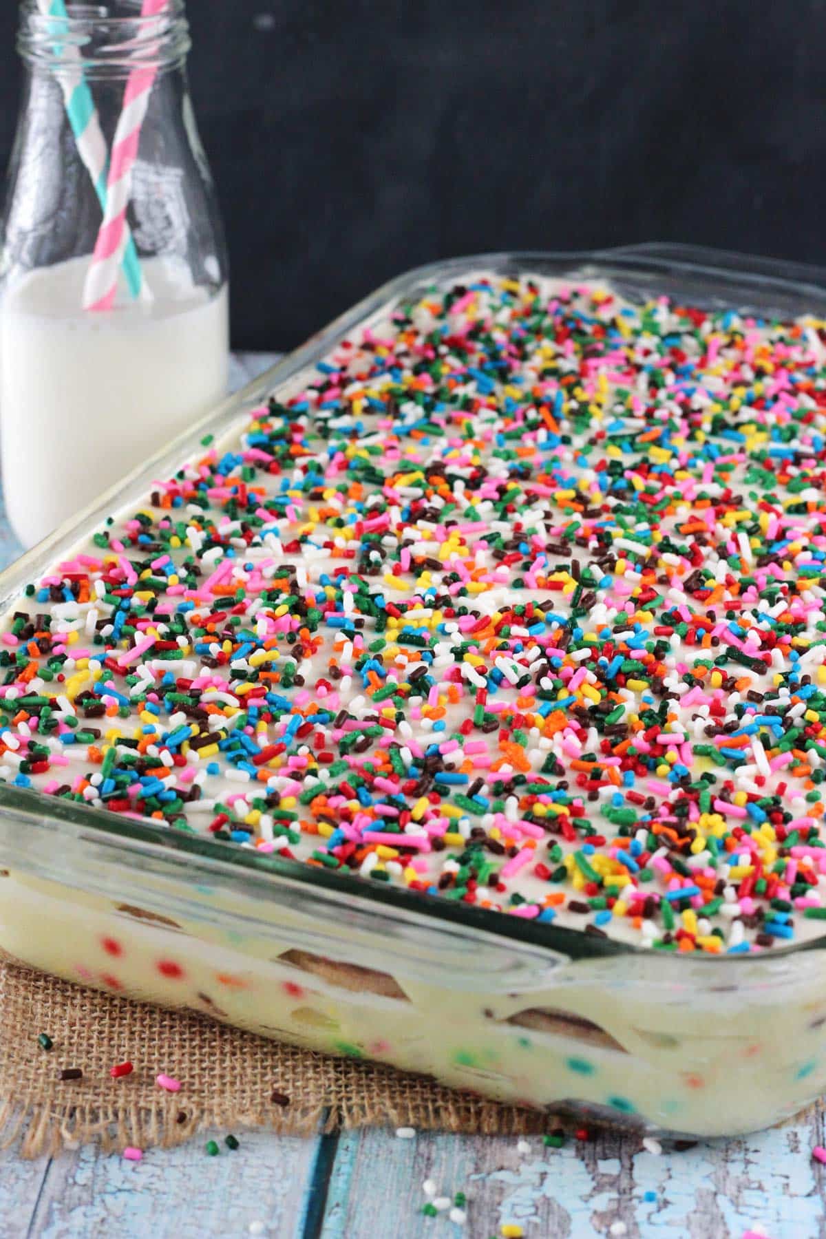 A Funfetti birthday cake icebox cake in a glass baking dish next to a bottle of milk.