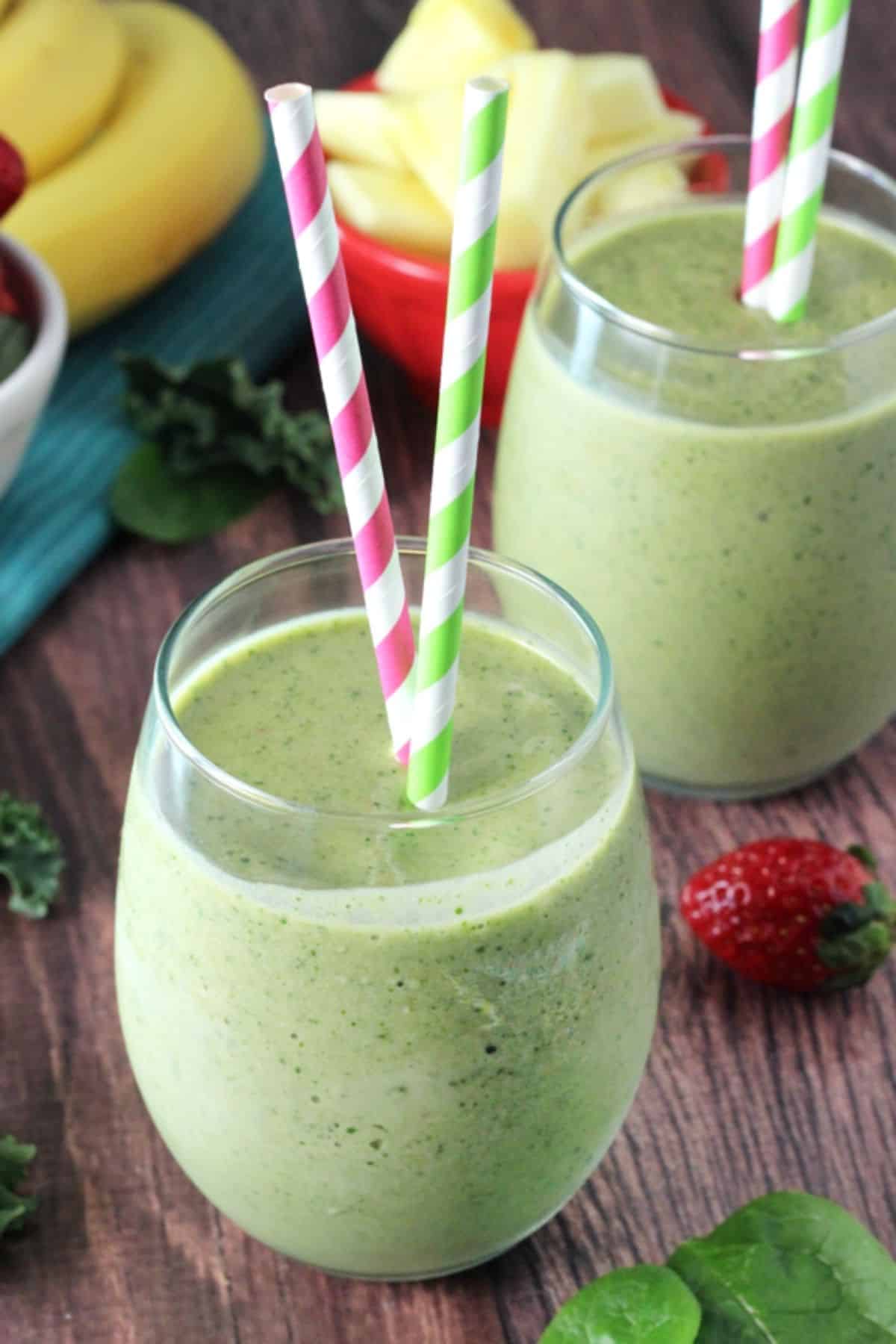 Two green smoothies in glass cups with colorful straws.