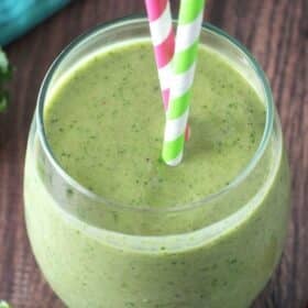 Top view of a green smoothie in a glass cup with colorful straws.