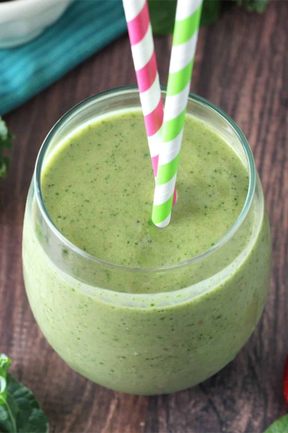 Top view of a green smoothie in a glass cup with colorful straws.