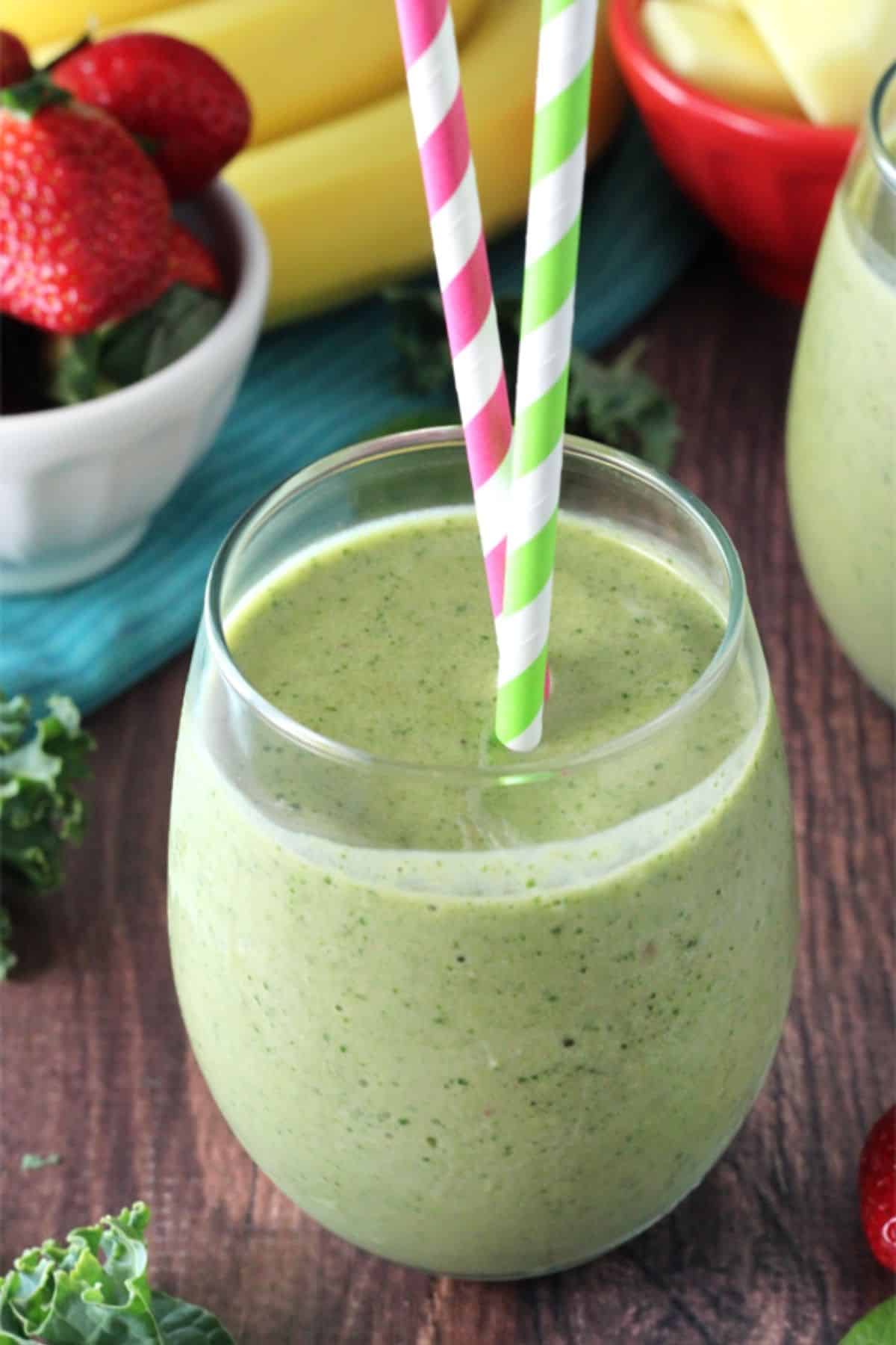 Close up of a green smoothie in a glass cup with colorful straws.