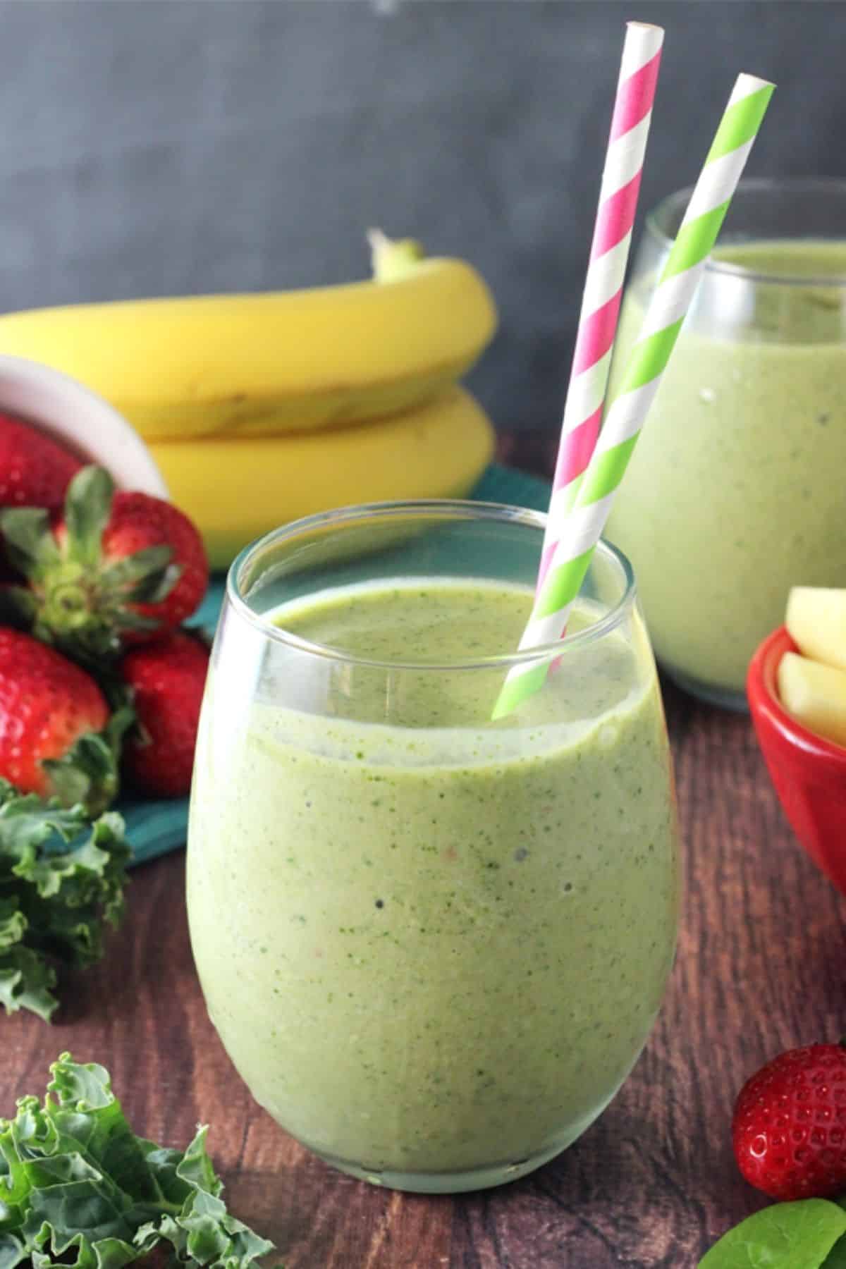 Close up of a green smoothie with colorful straws surrounded by fruit.