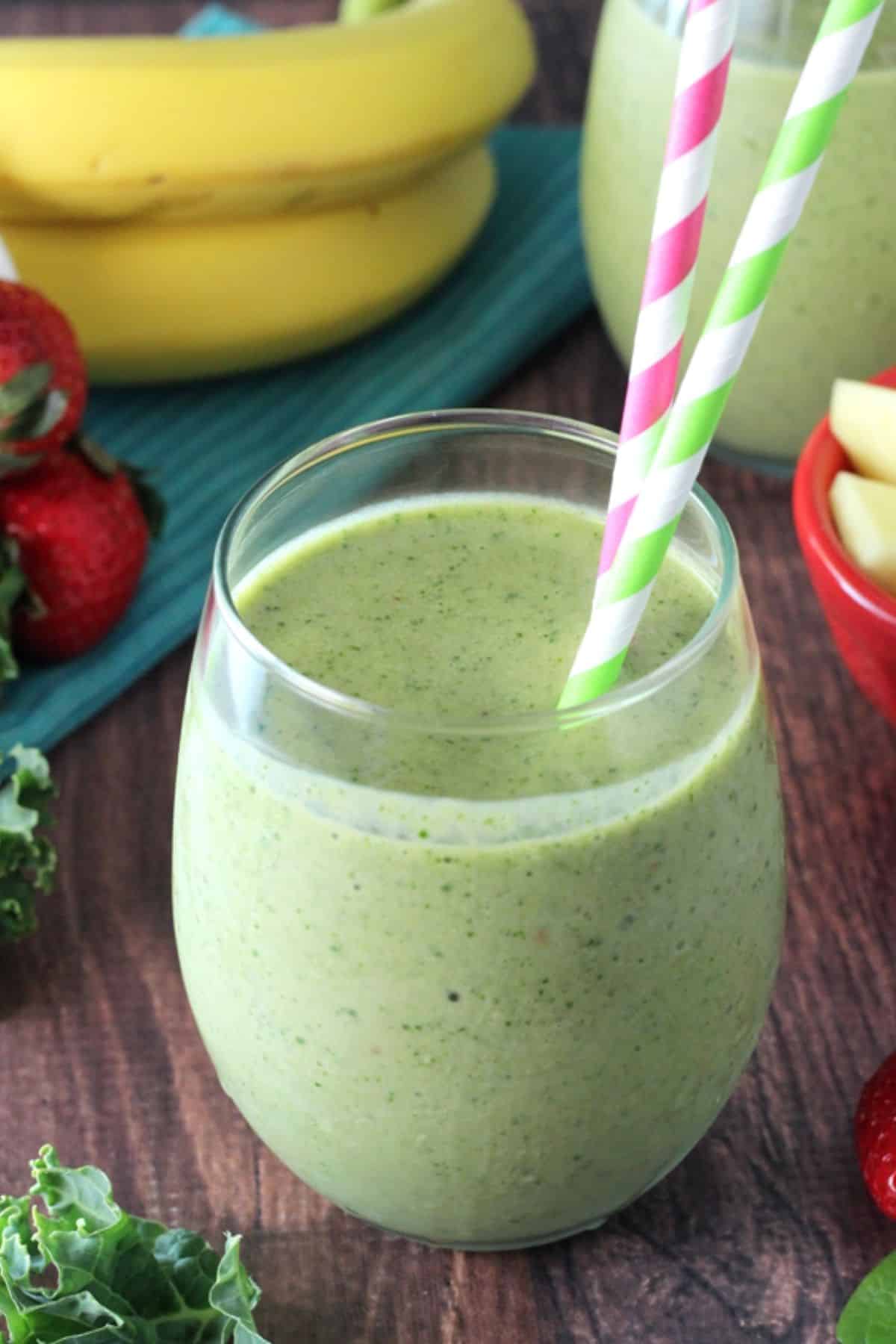 Close up of a green smoothie in a glass cup with colorful straws.