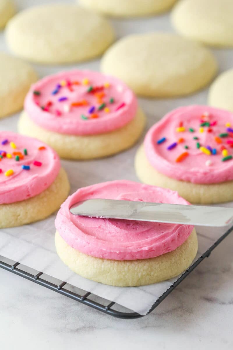 These copycat Lofthouse Cookies are soft and cakey with a melt-in-your-mouth texture and light flavor, just like the ones at the supermarket. Spreading pink buttercream on a cookie with a knife