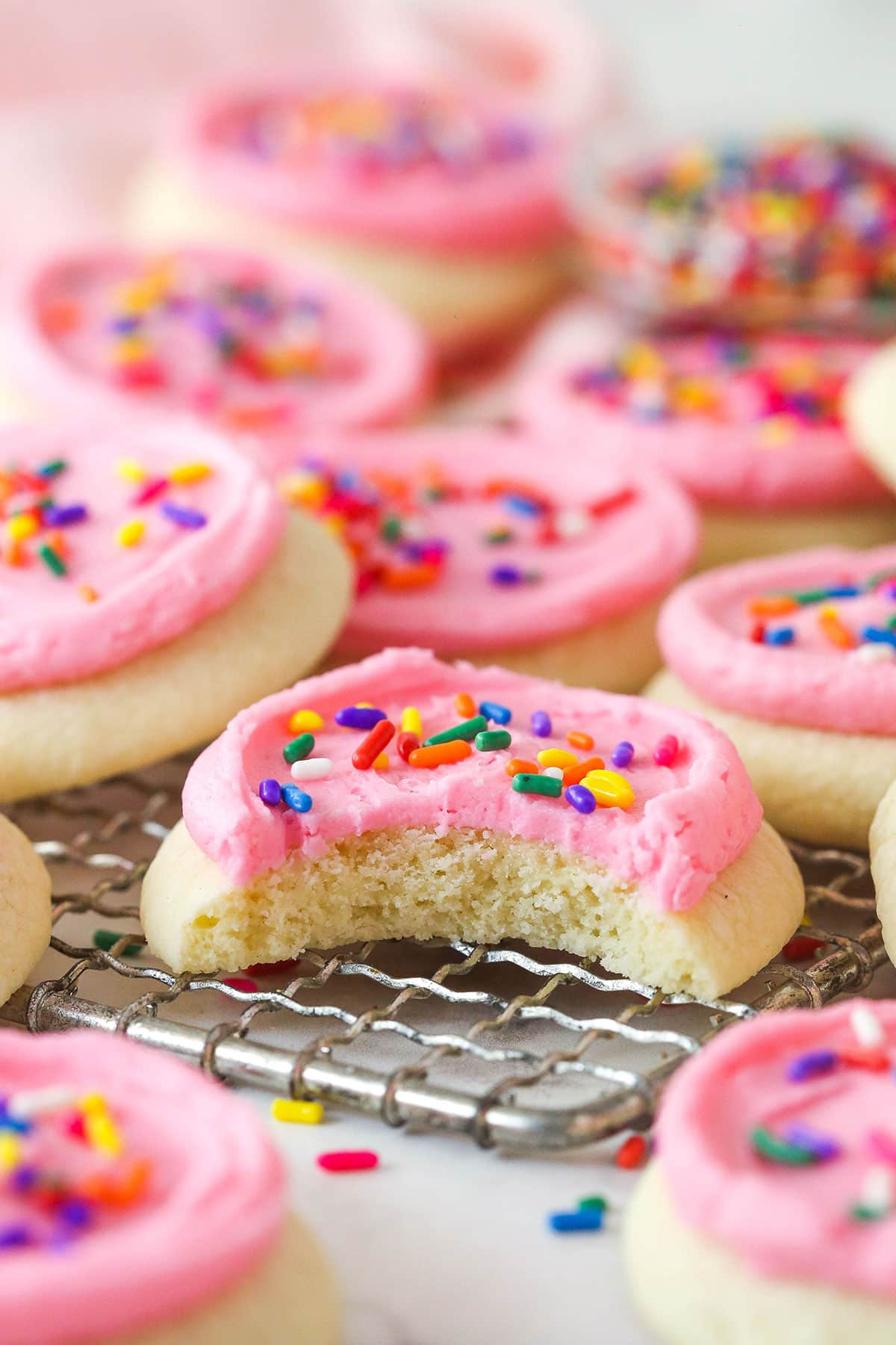 These copycat Lofthouse Cookies are soft and cakey with a melt-in-your-mouth texture and light flavor, just like the ones at the supermarket. Copycat Lofthouse cookies on a wire rack, one with a bite missing