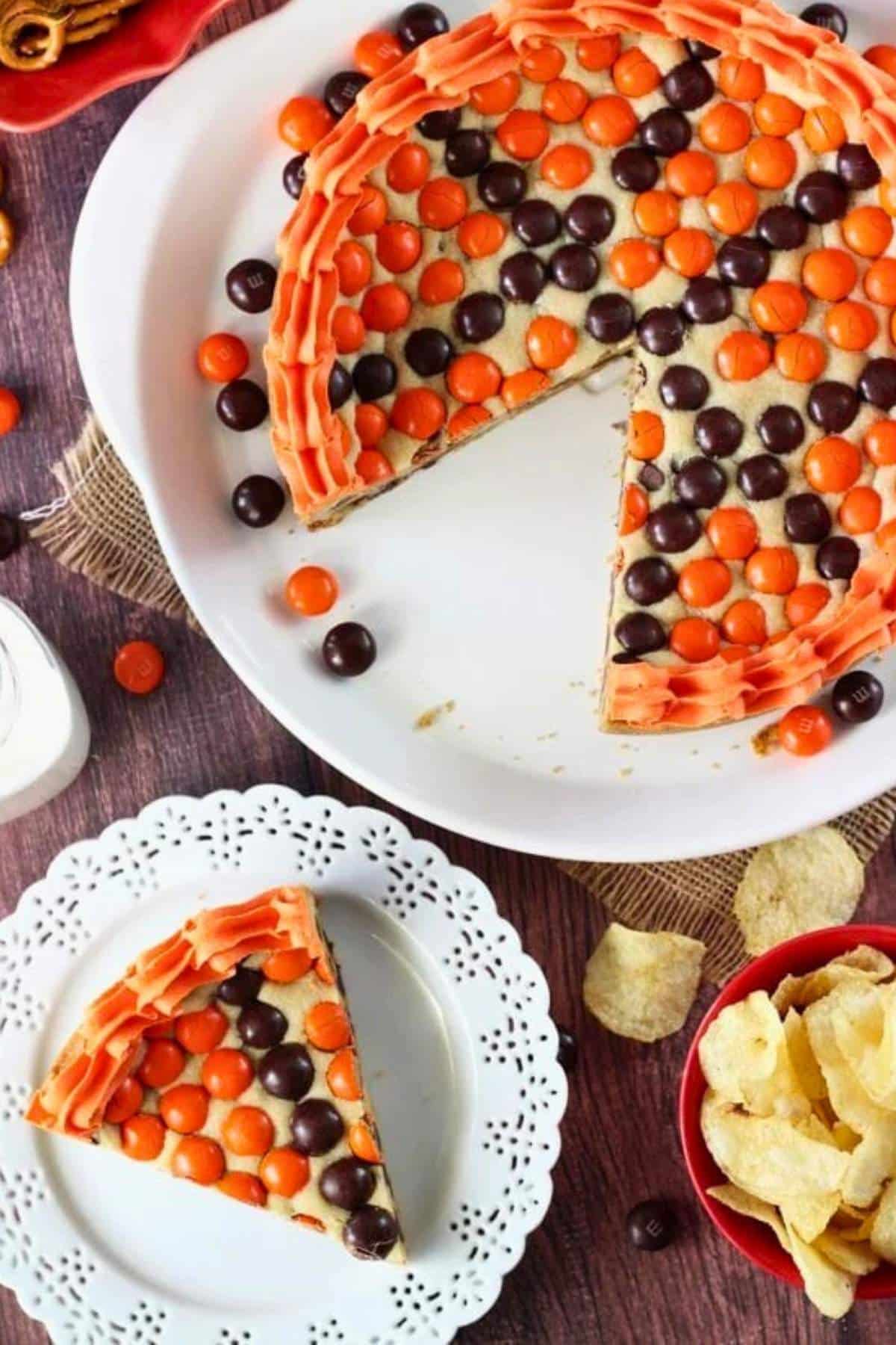 A slice of M&M basketball cake on a small white plate with the rest of the cake on a white platter.