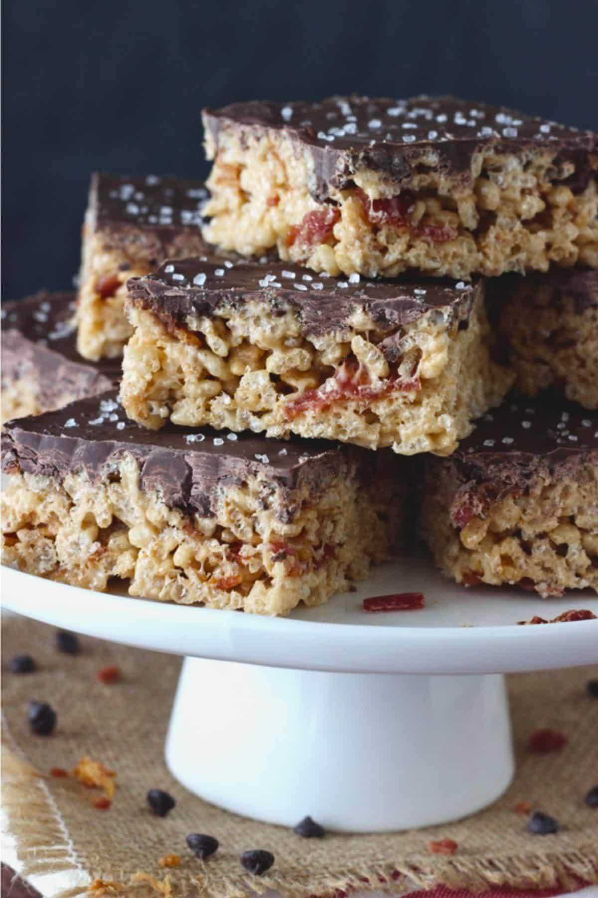 A stack of maple bacon rice krispie treats on a white cake stand.