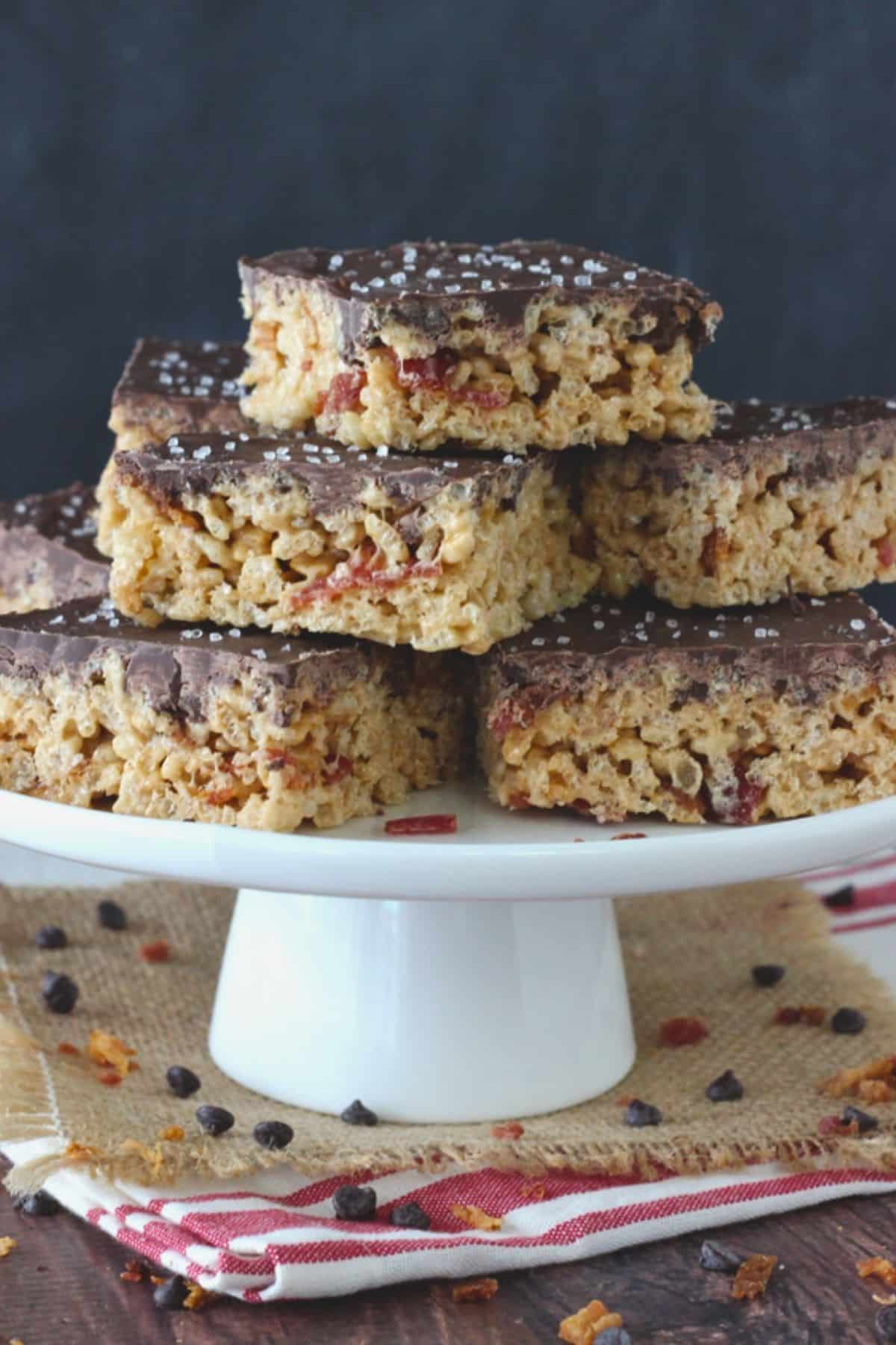 Close up of a white cake stand piled with maple bacon rice krispie treats.