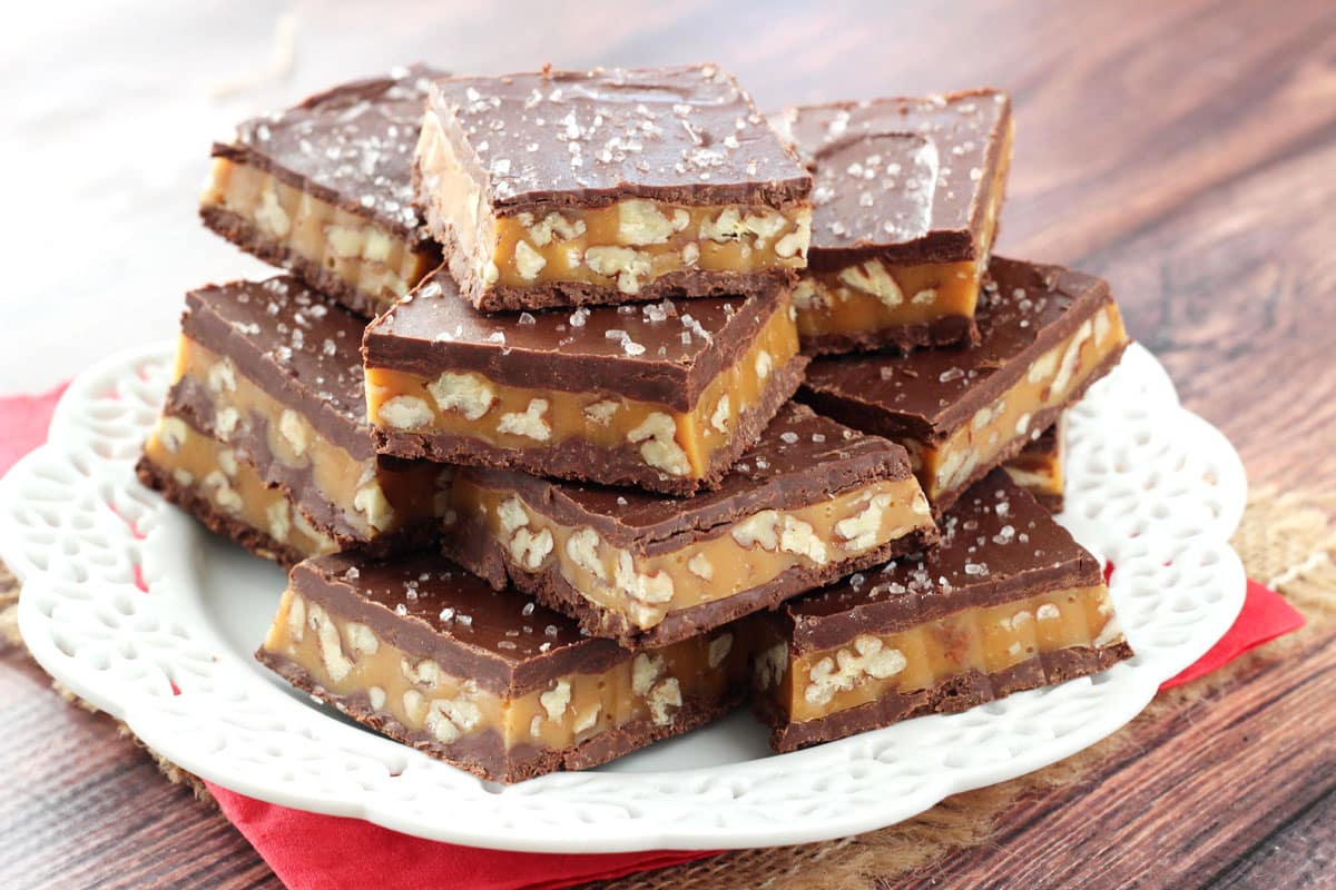 Pecan caramel turtle candy bars stacked in squares on a white plate.