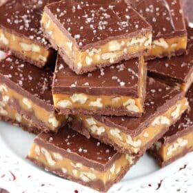 Close up of pecan caramel turtle candy bars stacked on a white plate.