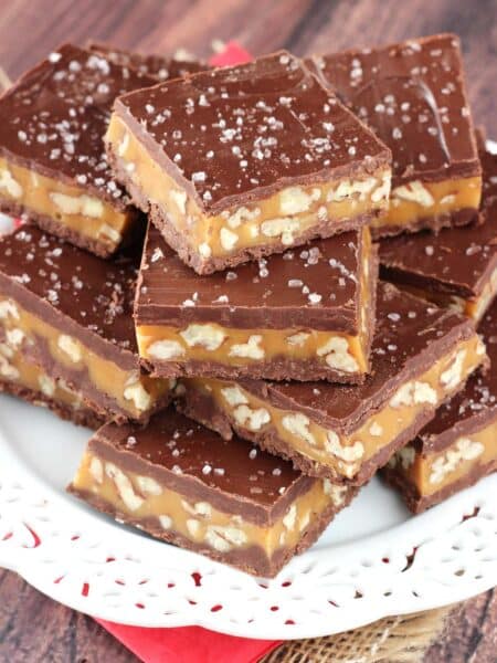 Close up of pecan caramel turtle candy bars stacked on a white plate.