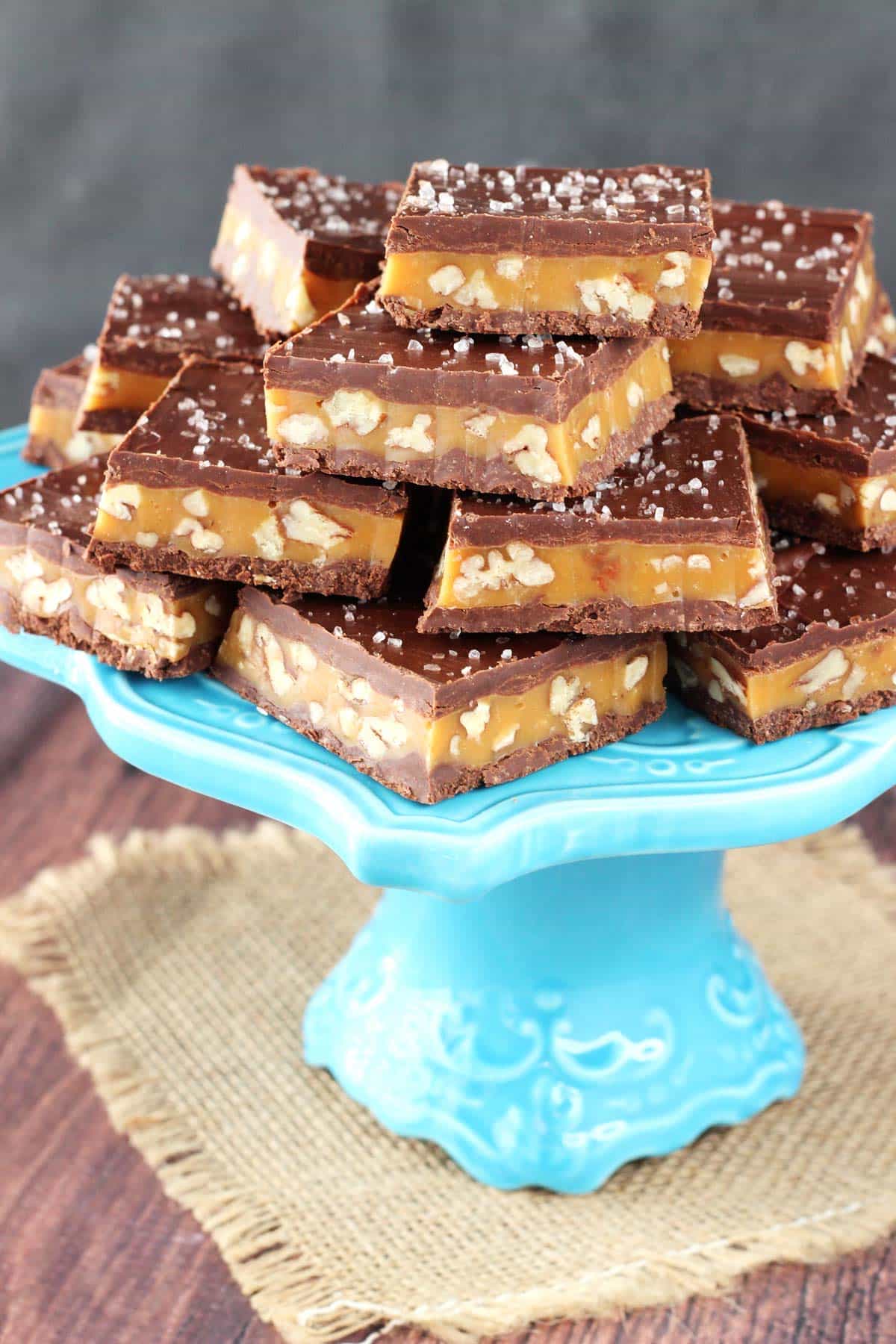 Pecan caramel turtle candy bars stacked on a light blue cake stand.