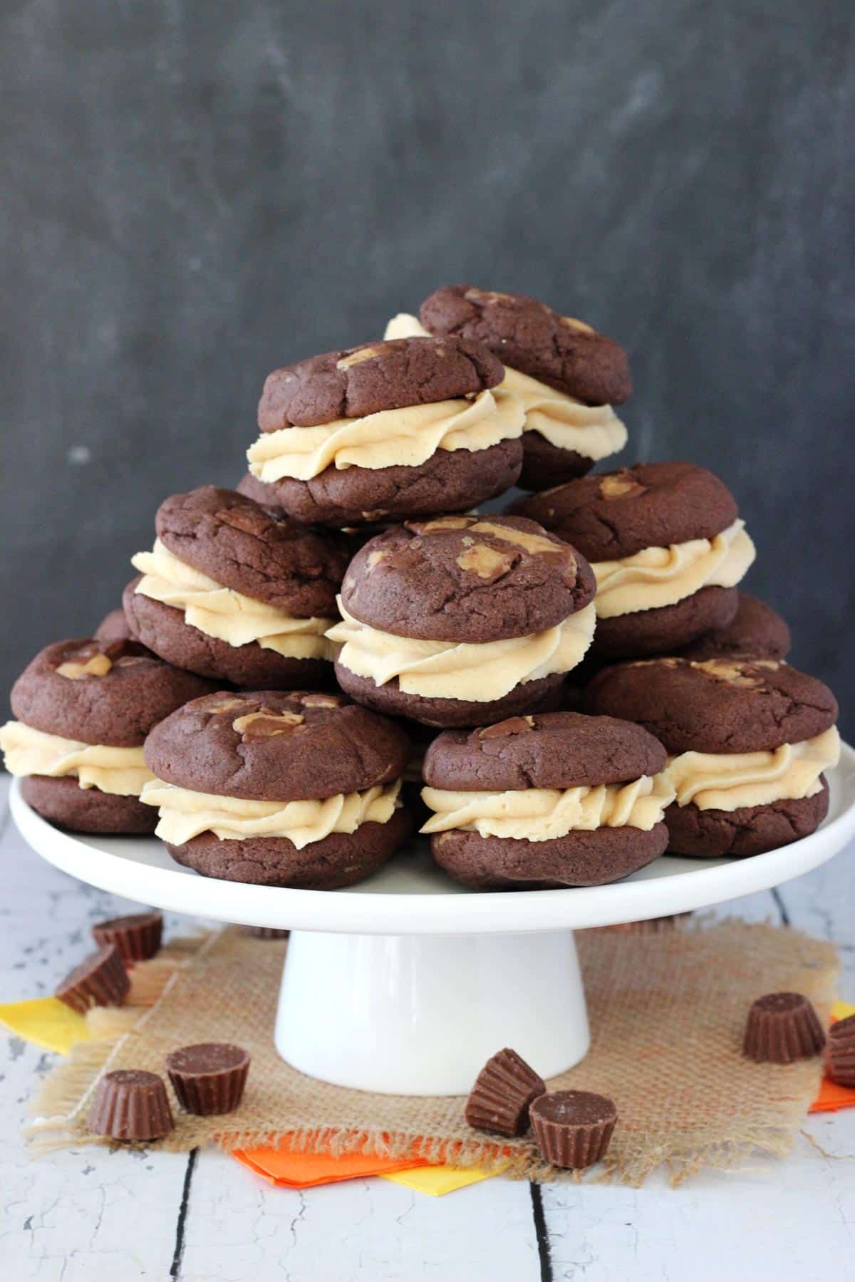 A white cake stand piled high with Reese's peanut butter cookie sandwiches.