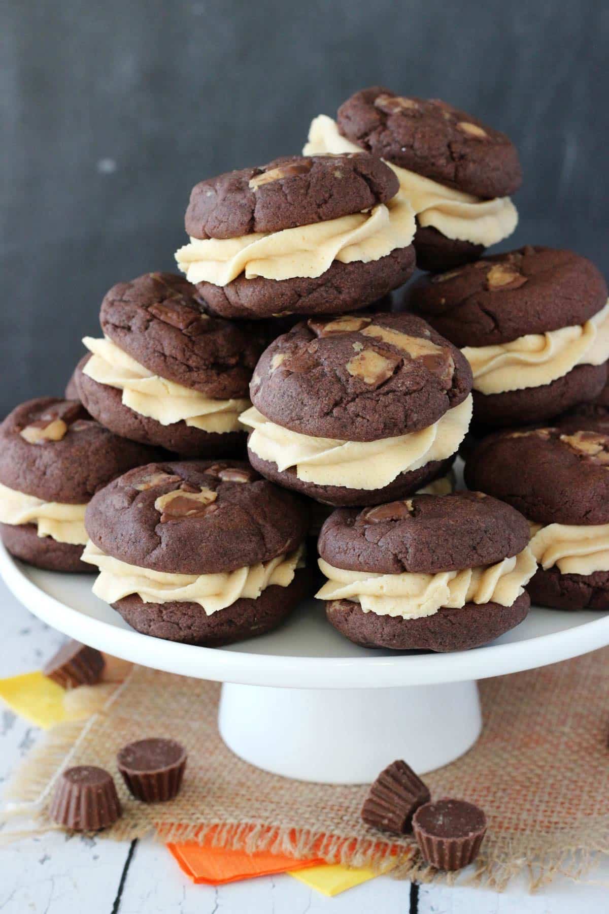 Side view of a white cake stand piled high with Reese's peanut butter cookie sandwiches.