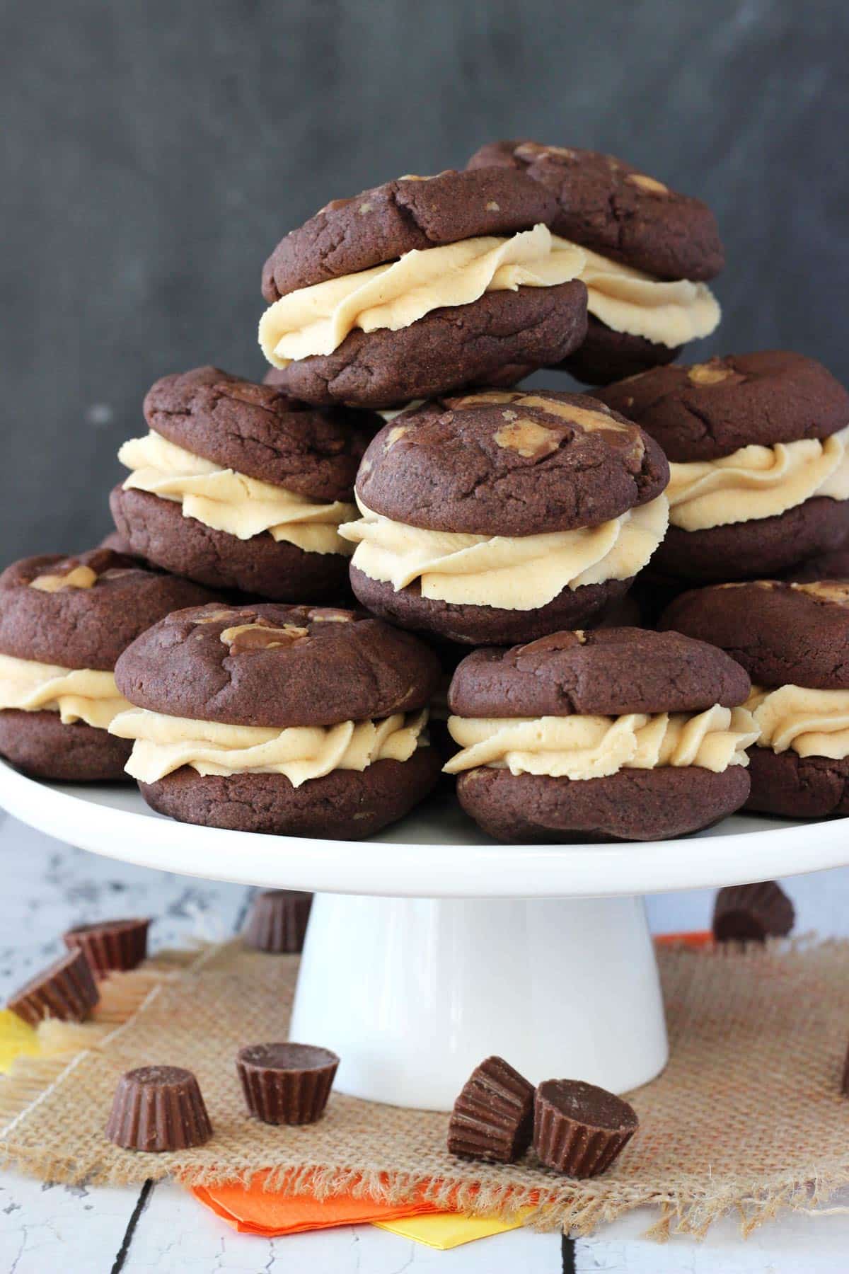 A white cake stand piled with Reese's peanut butter cookie sandwiches.