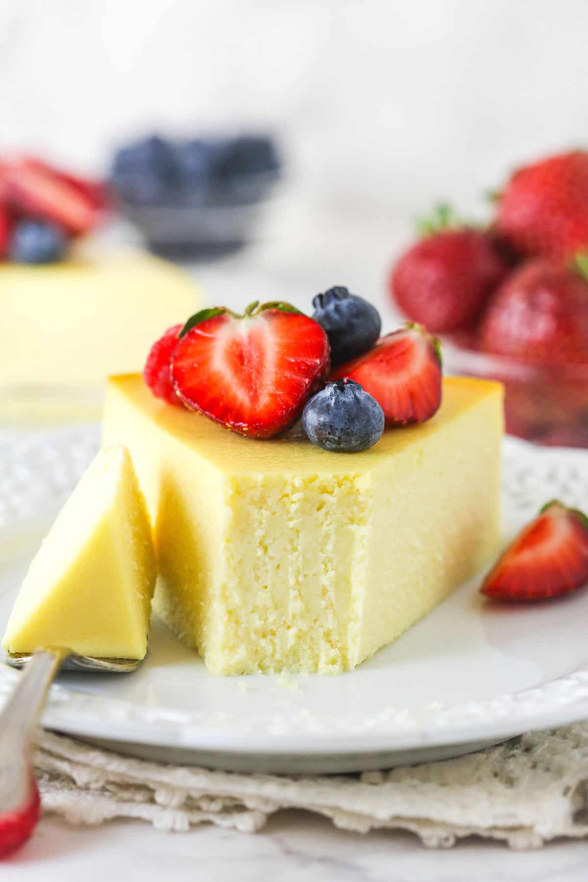 A slice of ricotta cheesecake on a plate with a bite on the fork next to it