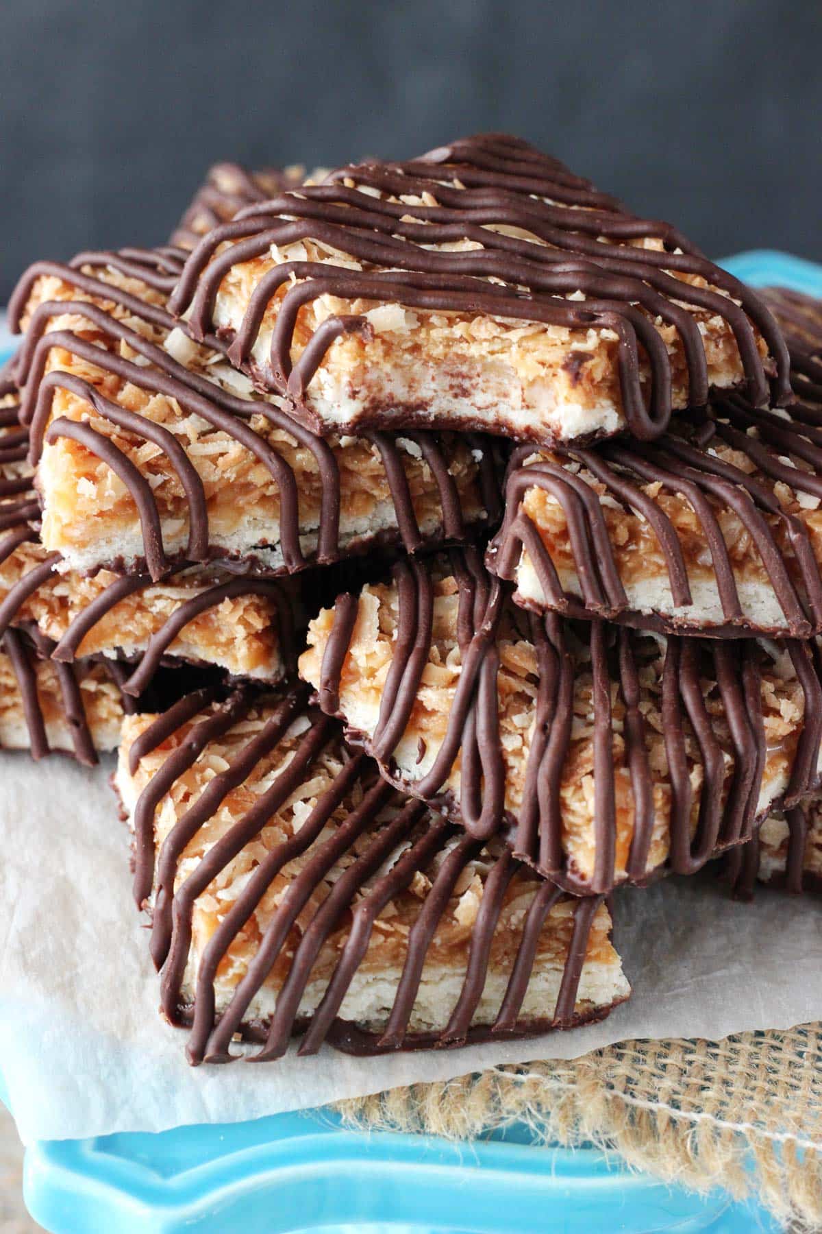Buttery shortbread cookies are topped with gooey caramel, nutty toasted coconut and rich chocolate in these heavenly Samoa Cookie Bars! Close up of a pile of Samoa Cookie Bars with a bite removed from top bar.