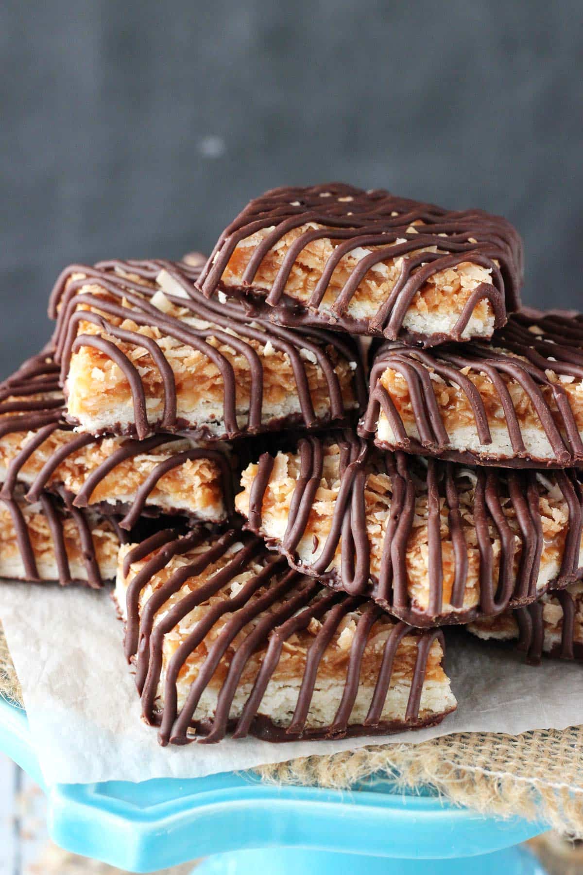 Close up of cut Samoa Cookie Bars piled on a blue stand.