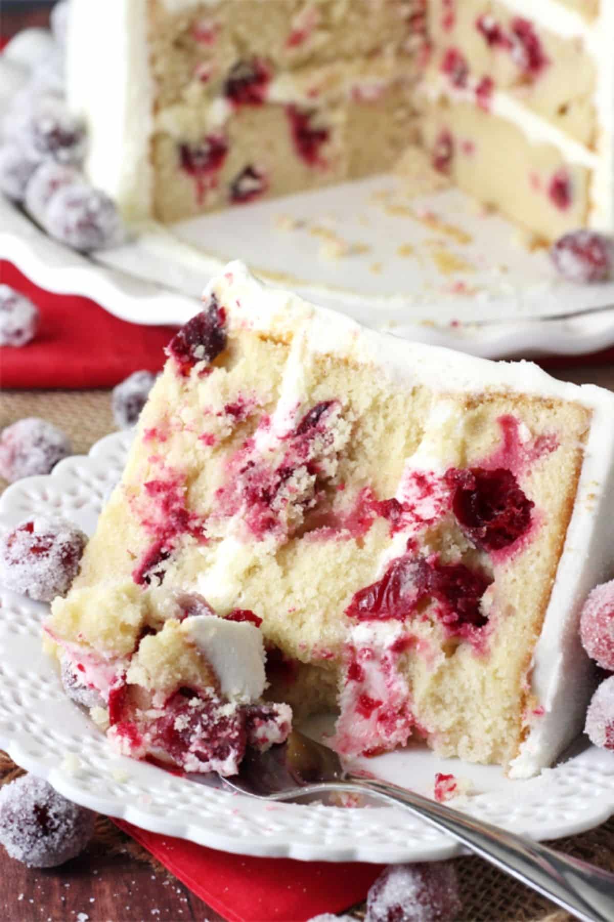 A slice of white chocolate cranberry cake on a white plate with a bite removed on a fork.