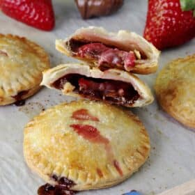 Baked strawberry Nutella hand pies on a piece of parchment with the top pie cut in half to show center.