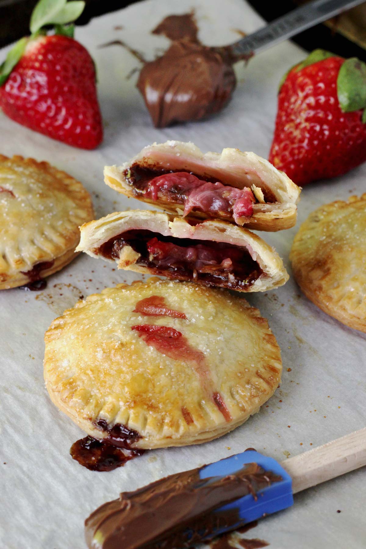 Baked strawberry Nutella hand pies on a piece of parchment with the top pie cut in half to show center.