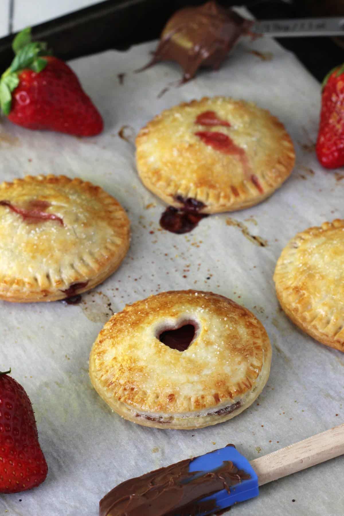 A few baked strawberry Nutella hand pies on a piece of parchment.