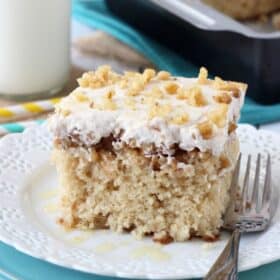 A slice of baklava poke cake on a white plate next to a fork.